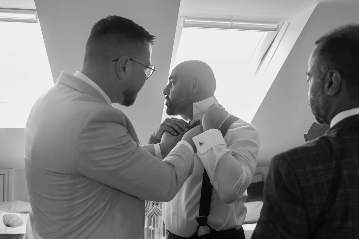 Groomsmen helping groom to do up his bow tie.