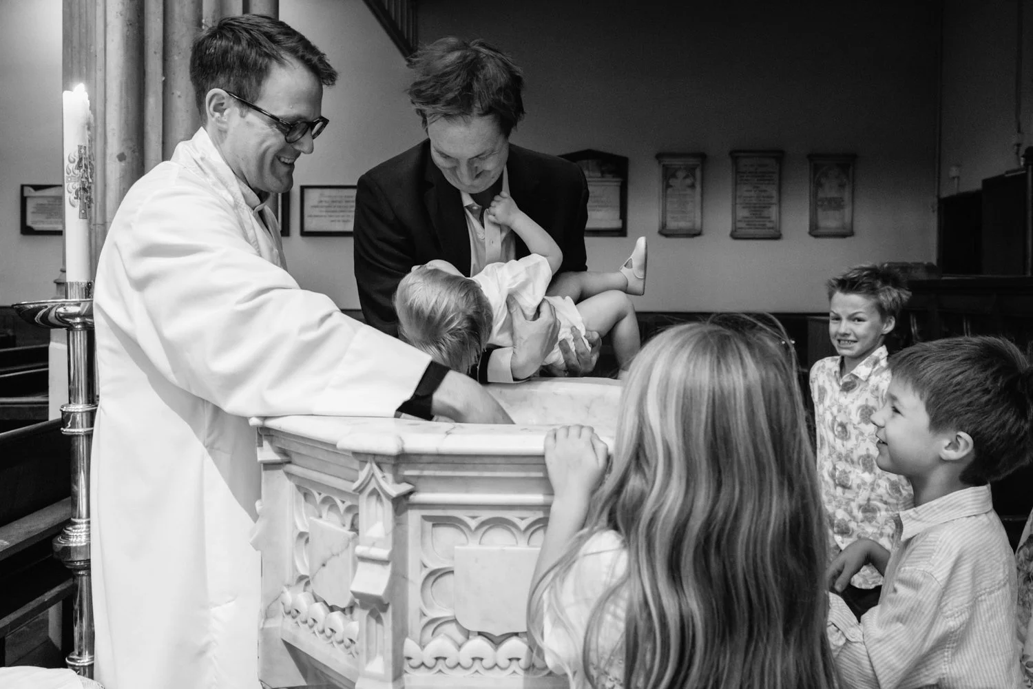 Father lowers baby son towards the font for the christening moment.