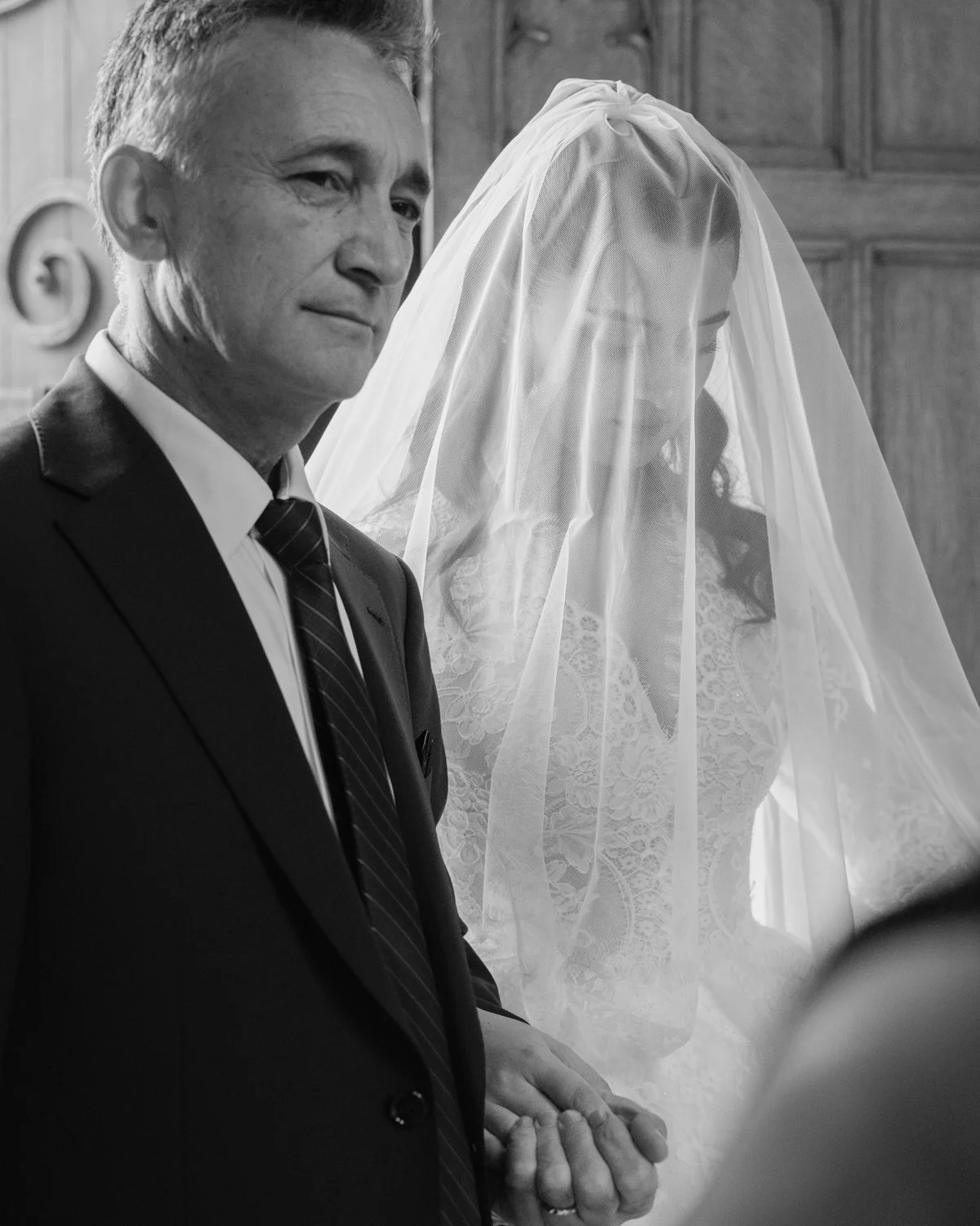 Father entering church with his daughter covered in a veil, and both looking thoughtful.