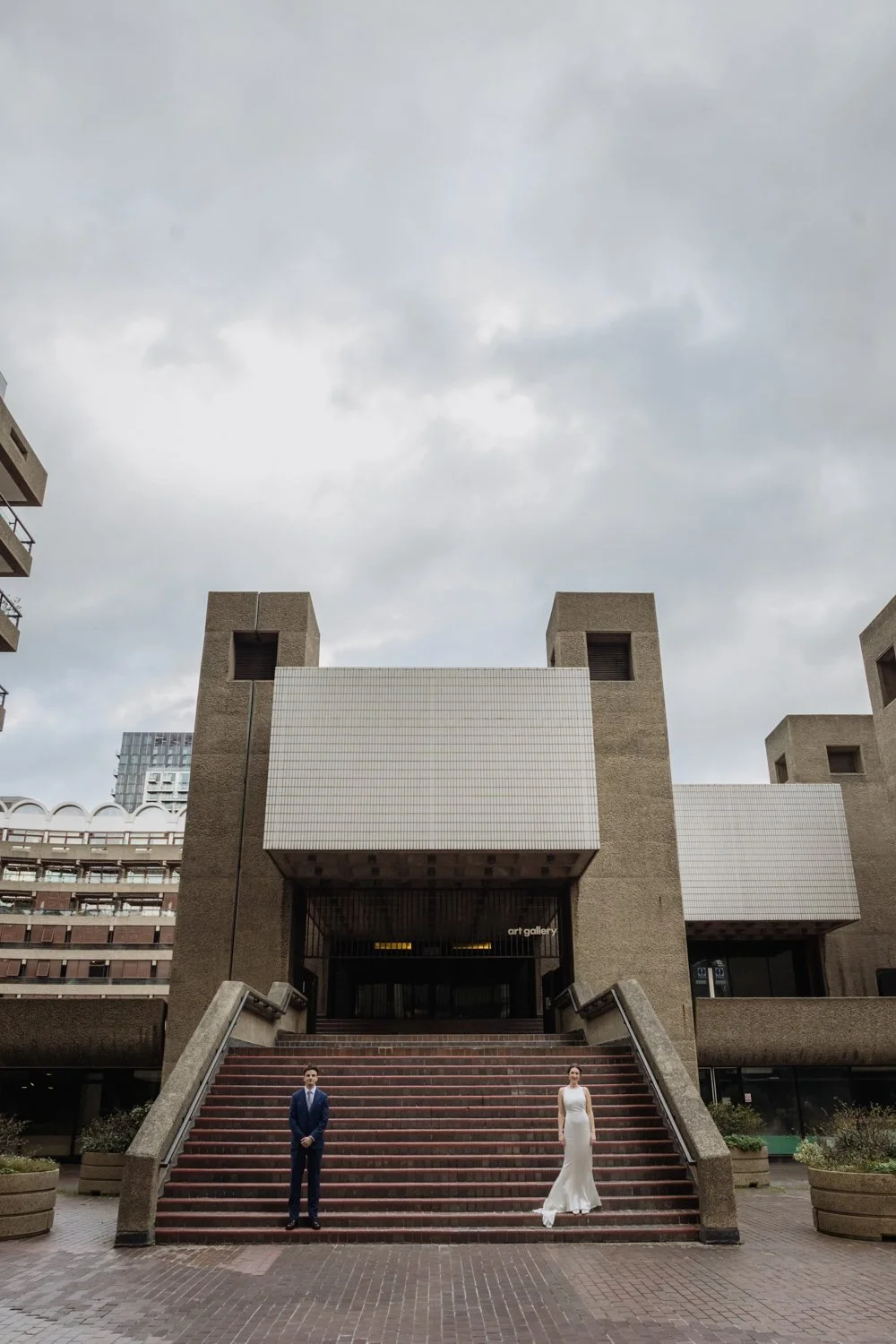 Bride and Groom stylised portrait with them standing either side of the steps leading up to the Barbican Art Gallery.