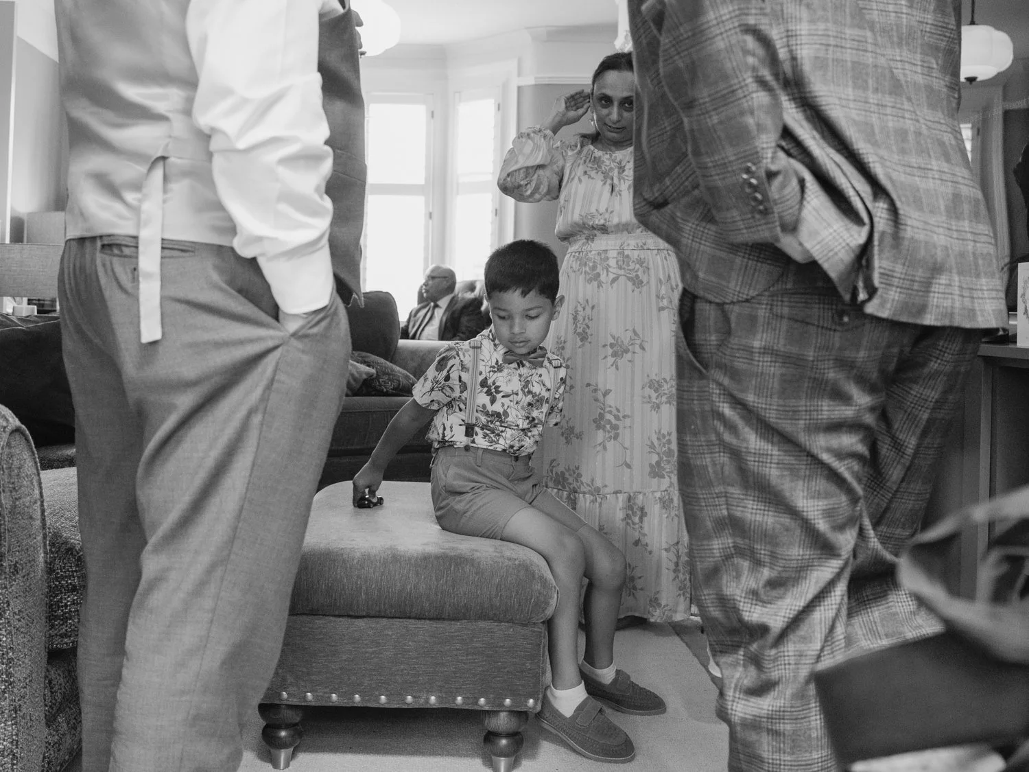 Boy with toy car sitting amongst adults during bridal prep.