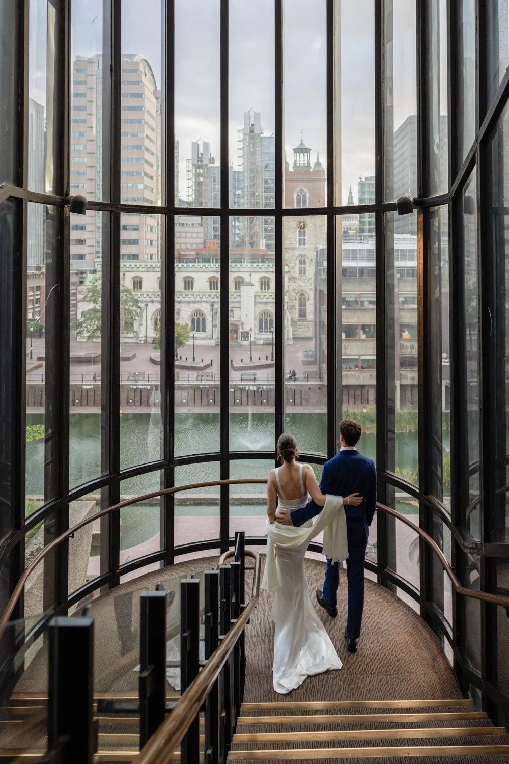 Bride and Groom on the staircase on level 3 of the Barbican looking out at the view of St Giles Church and the lakeside.
