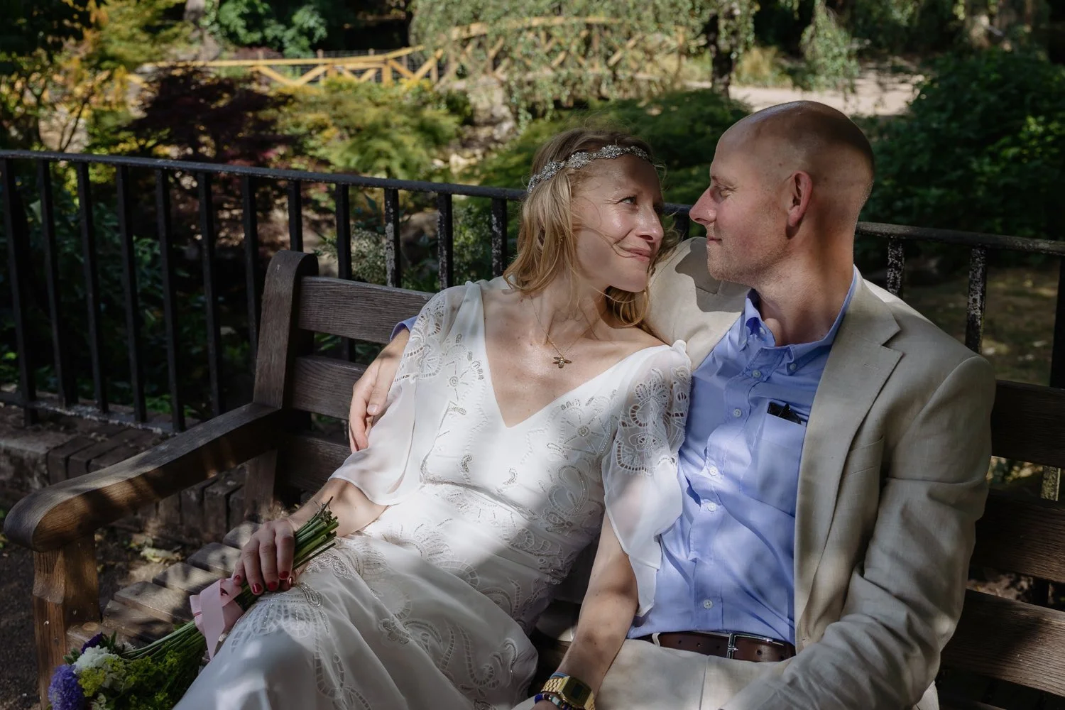 Bride and Groom relaxing on a bench and looking at each other with love.