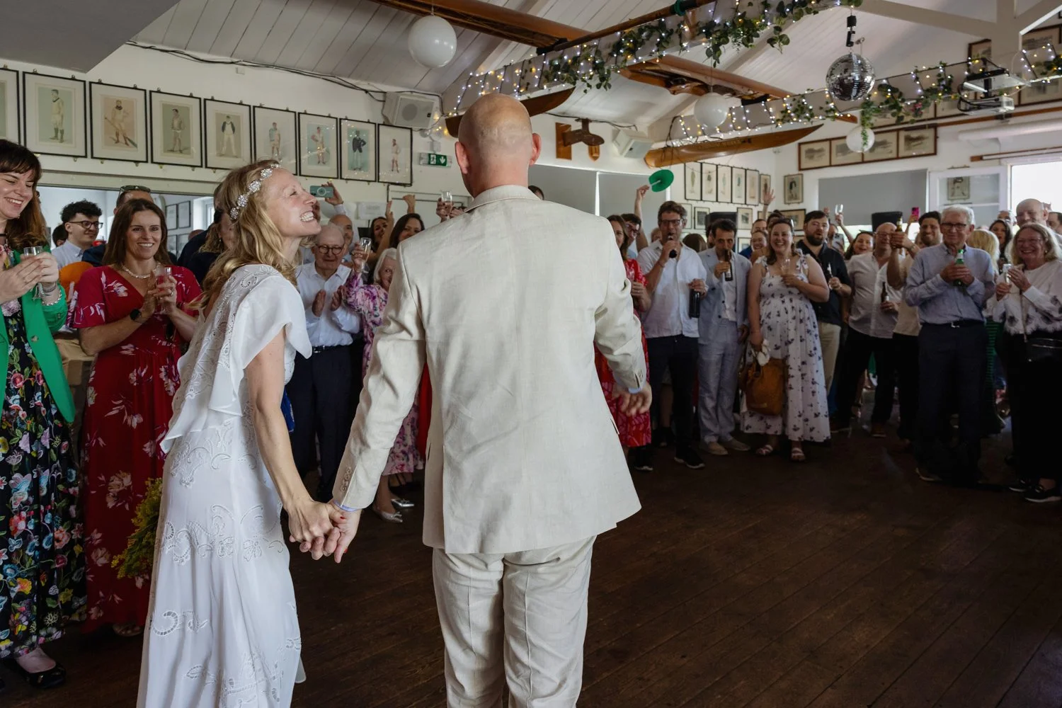 Bride smiles at groom with their wedding guests cheering them in at Twickenham Rowing Club.