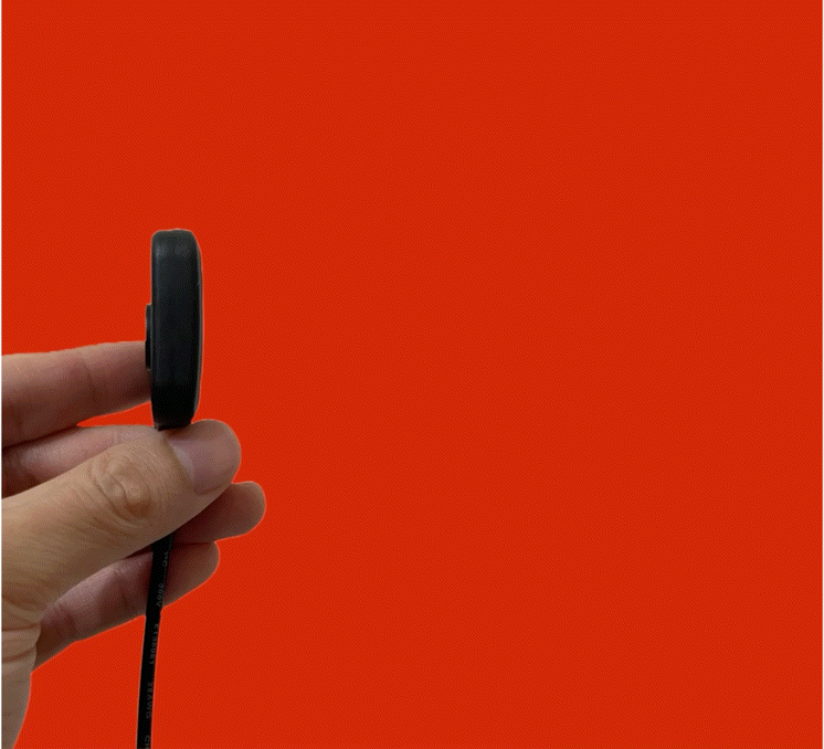 Close-up of a hand holding a small black wireless earbud against an orange background.