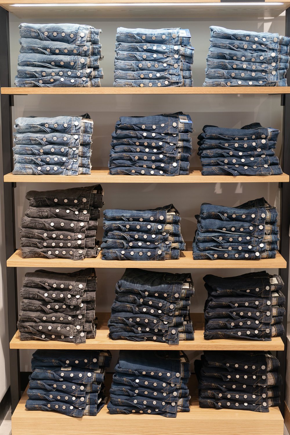 Stacks of folded jeans on wooden shelves in various shades of blue and black.
