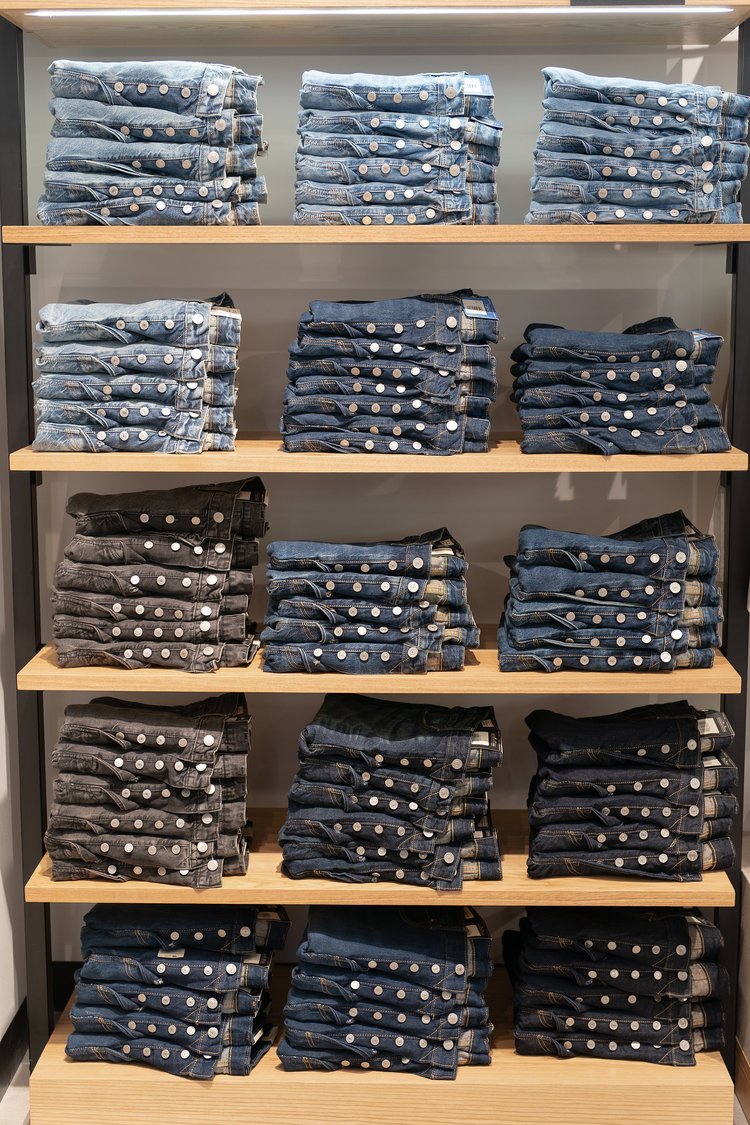 Stacks of folded jeans on wooden shelves in a clothing store.