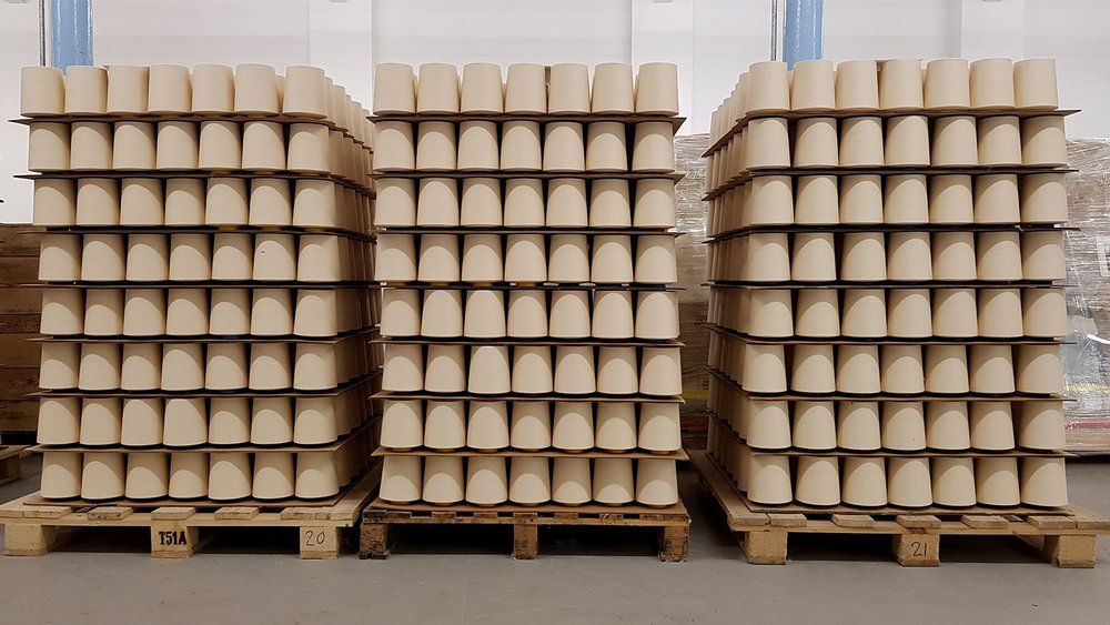 Pallets stacked with cones of spun cotton yarn in a mill warehouse.