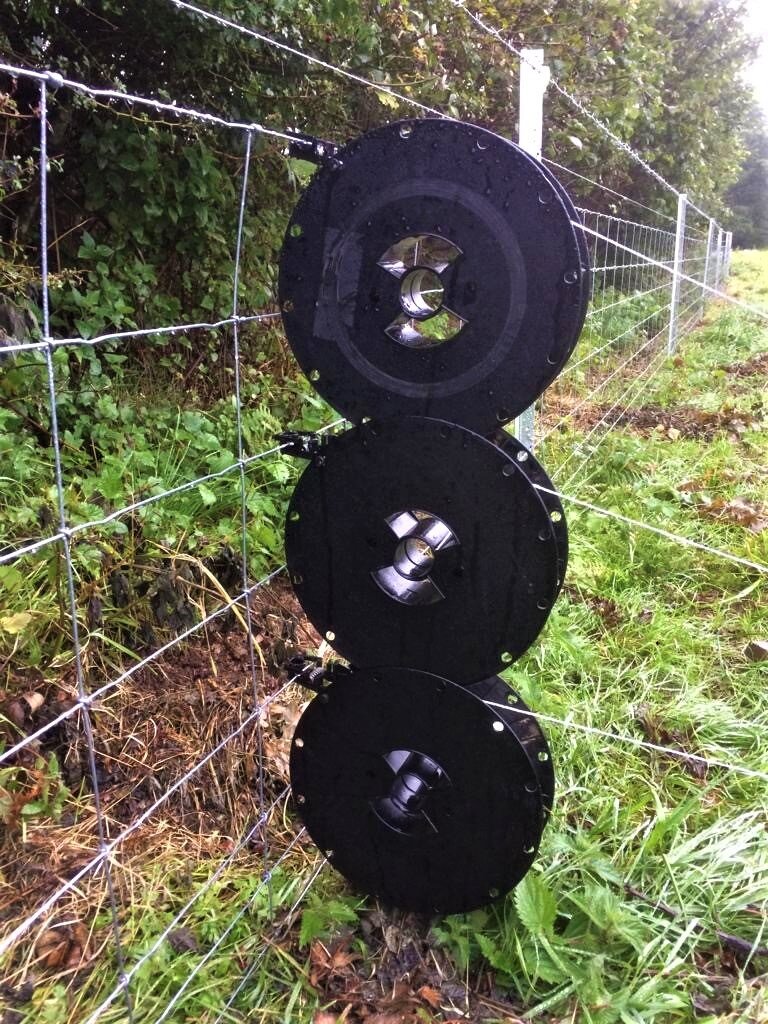 Kiwitech Spools and wire connected to a fence using release hooks in a grass field.