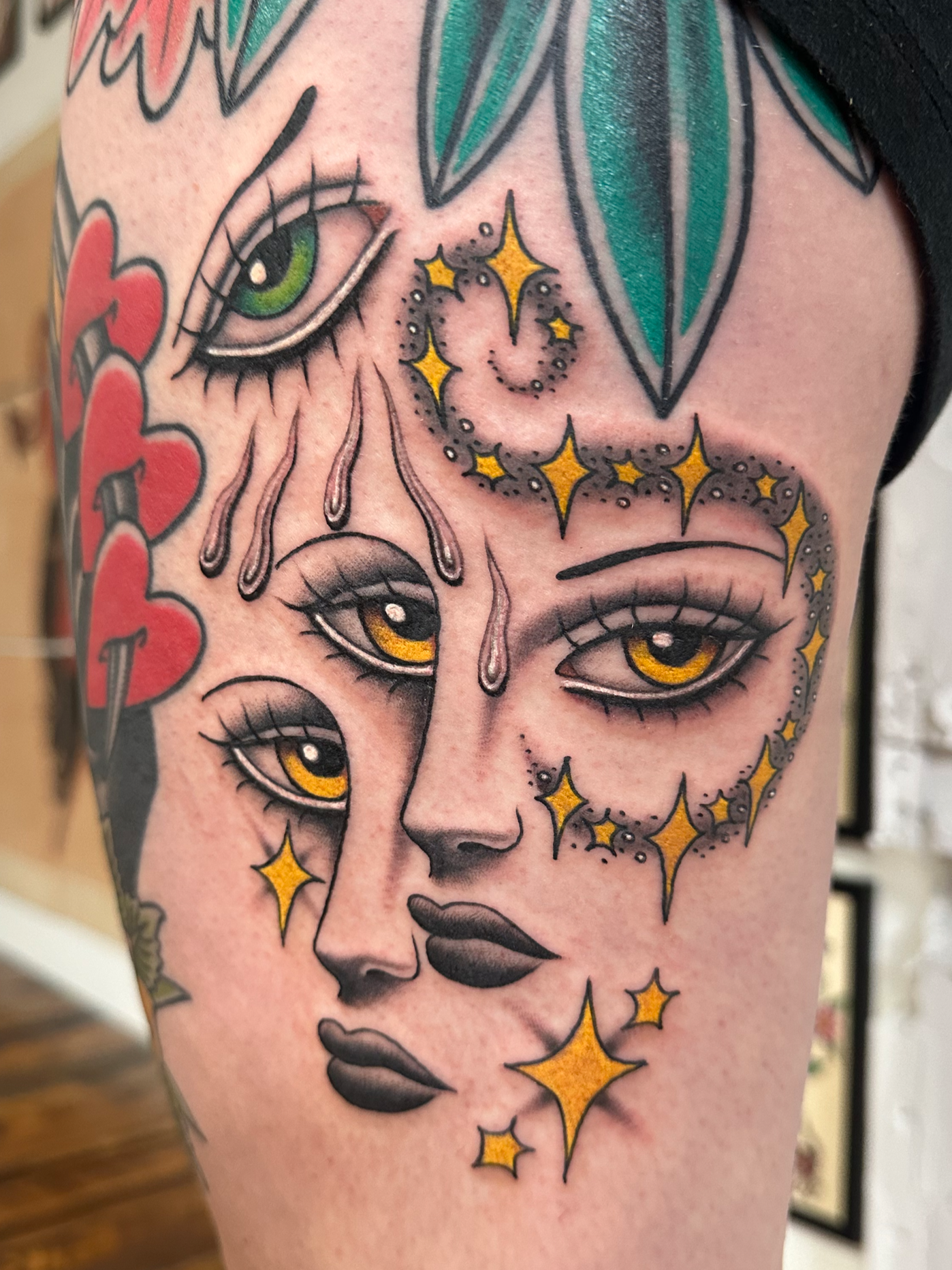 Tattoo of a woman's face with green eyes, surrounded by stars and water drops, with colorful leaves at the top.