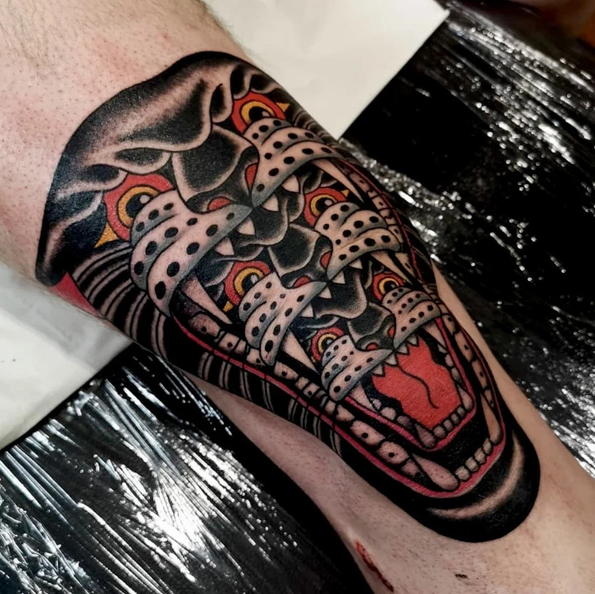 Knee tattoo of a panther with two other panthers inside mouth.