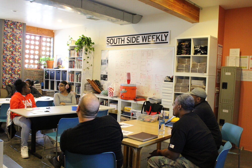  3 adults listening to 4 students sitting at tables in South Side Weekly office. Credit: Mae Morris 