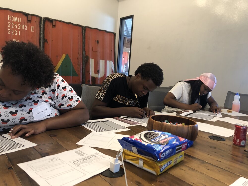  Three students working on drawings at a wooden table with a box of Oreos in the middle.  