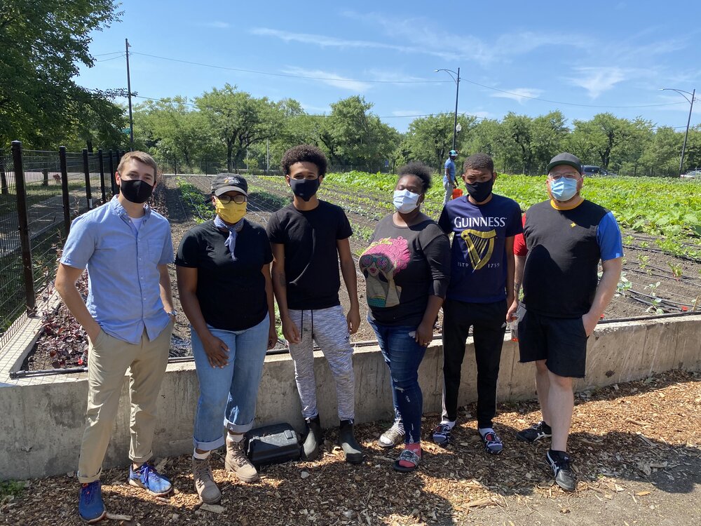  A group of people wearing masks standing in front of a large garden plot.  