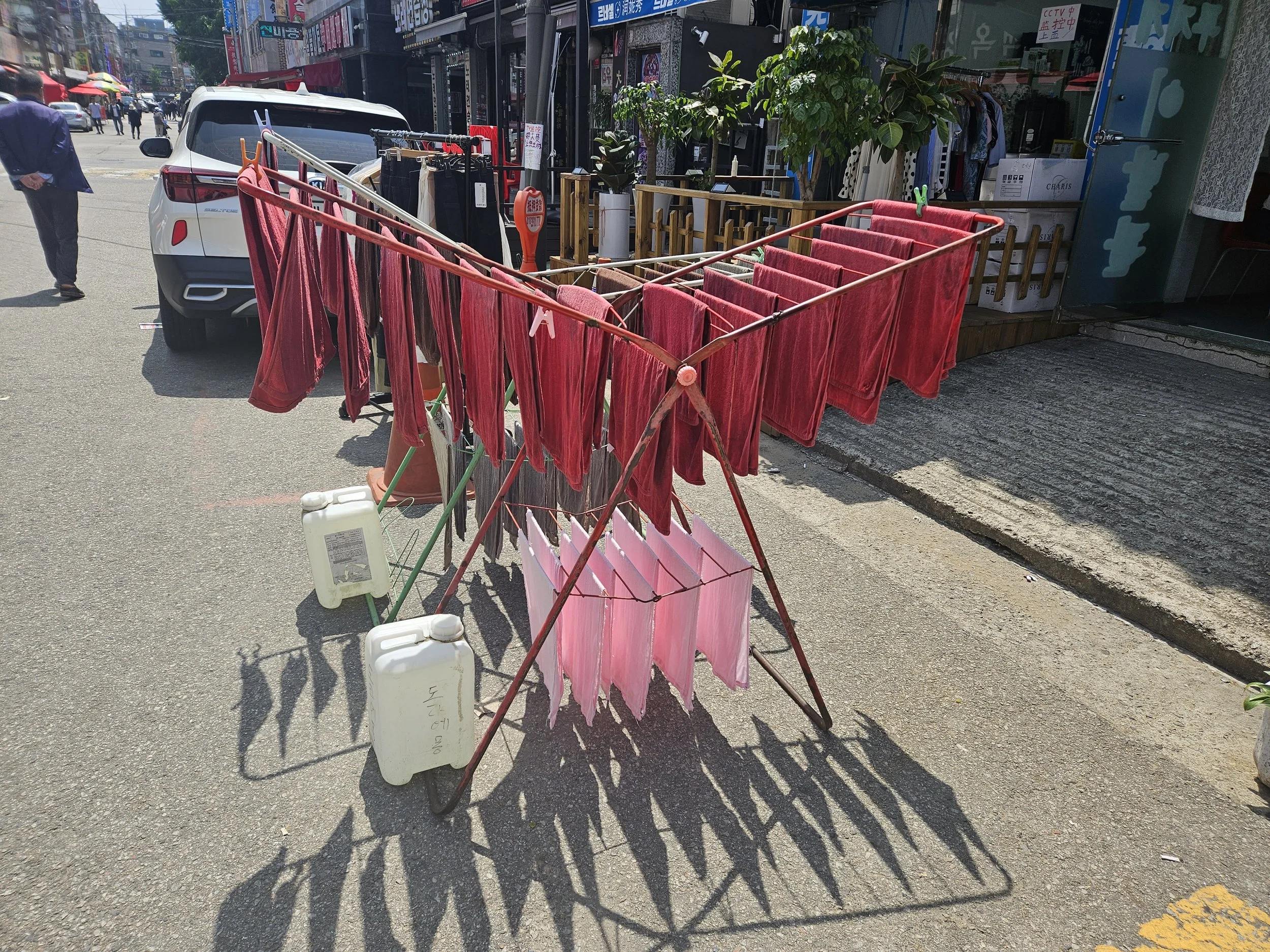 Towels are hung on a worn metal drying rack with a plastic container filled with water holding the rack in place. ruby red towels are hung on the top while flamingo pink are hung on the bottom.