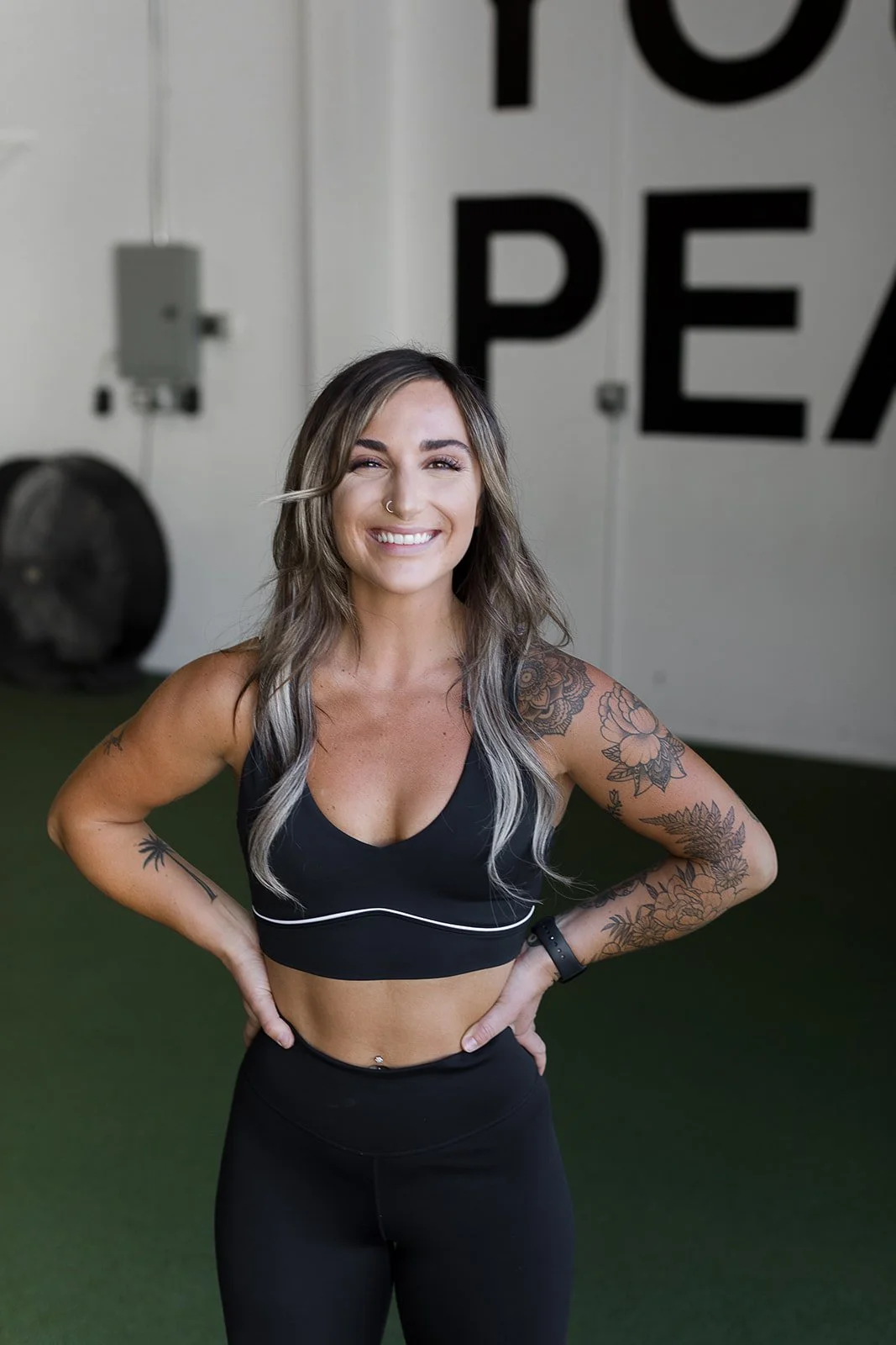 Woman with tattoos and piercings in gym attire smiling in a fitness center.