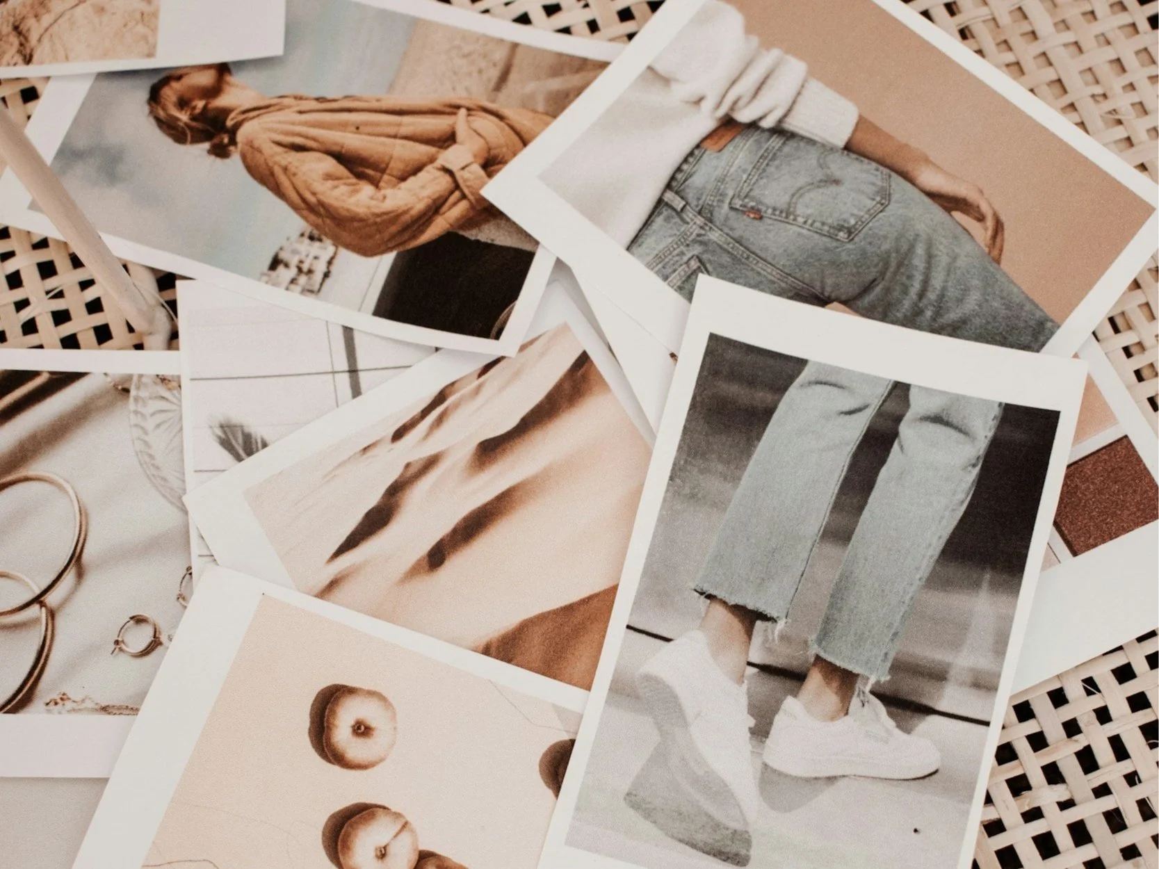 Various printed photos scattered on a surface, including a woman in a tan sweater, close-up of fabric and jewelry, desert dunes, and a person wearing ripped jeans and white sneakers.