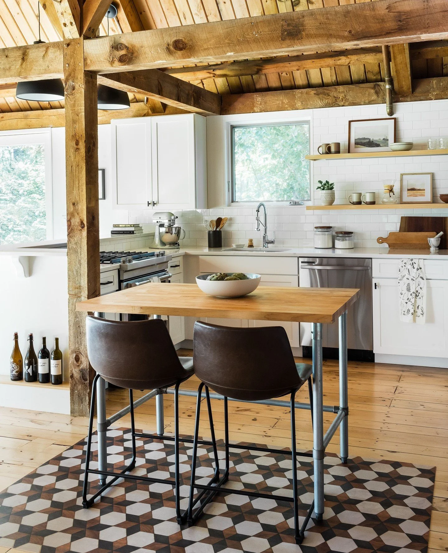 Original timber posts and a cathedral pine ceiling frame a kitchen that is otherwise clean and entirely functional &mdash; white shaker cabinetry, white quartz countertops, a subway tile backsplash, and open maple shelving. A pipe-leg butcher block i
