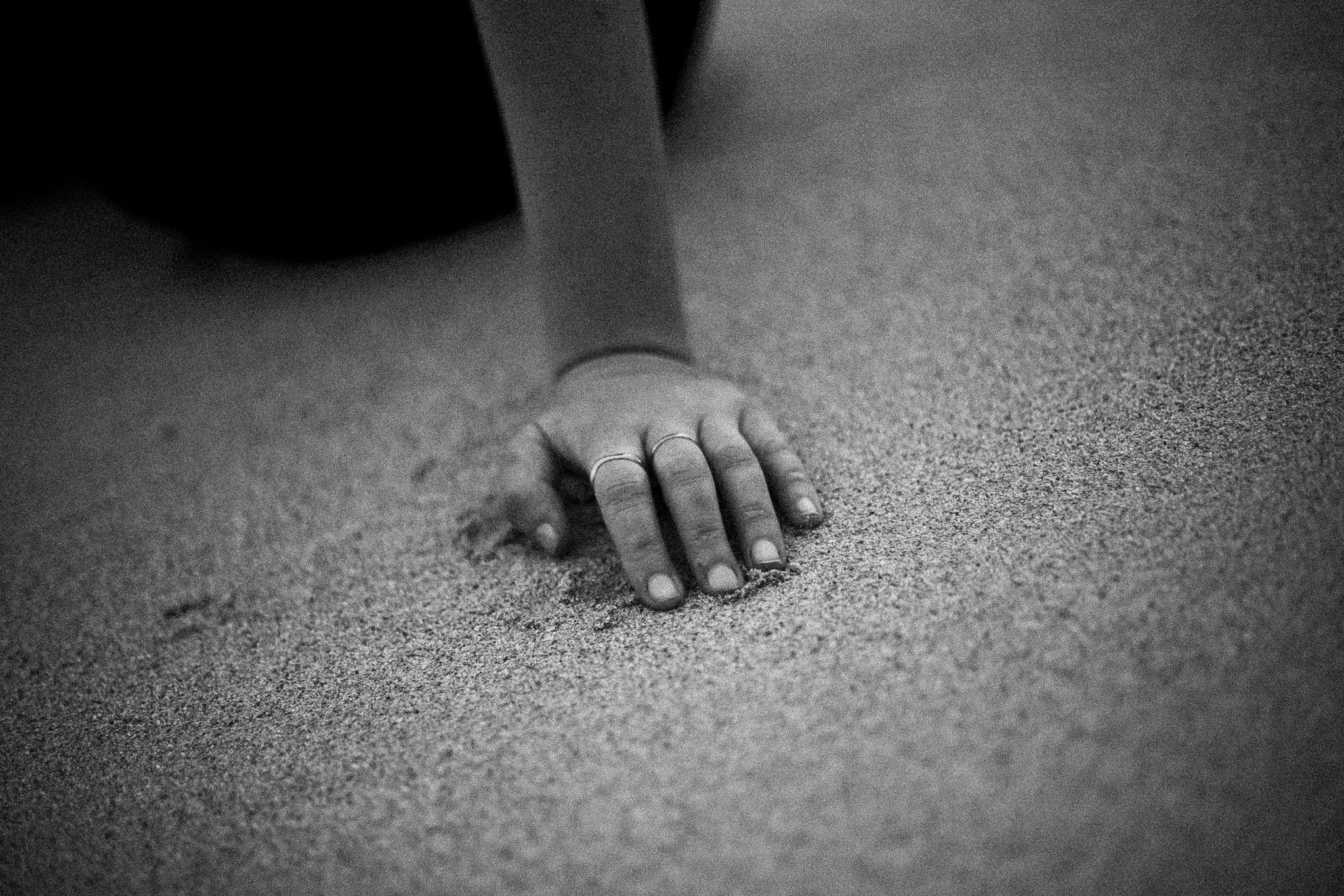 Une main repose sur le sol, probablement de la plage, en noir et blanc.