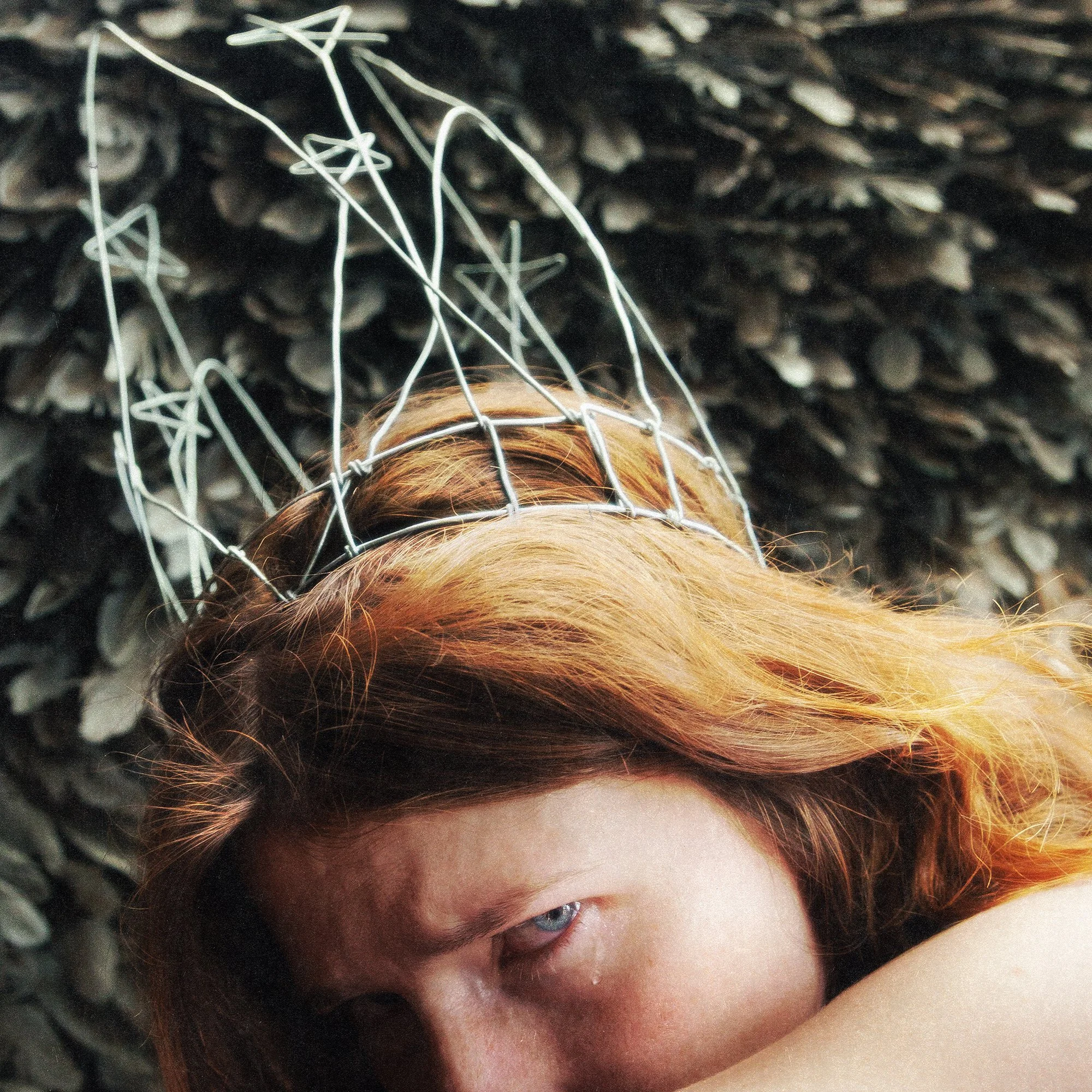 Close-up of a person's face with red hair, lying down on a textured dark surface, partially covered by someone else's head, with visible eye and forehead. Cayley Spivey album art for Carson.