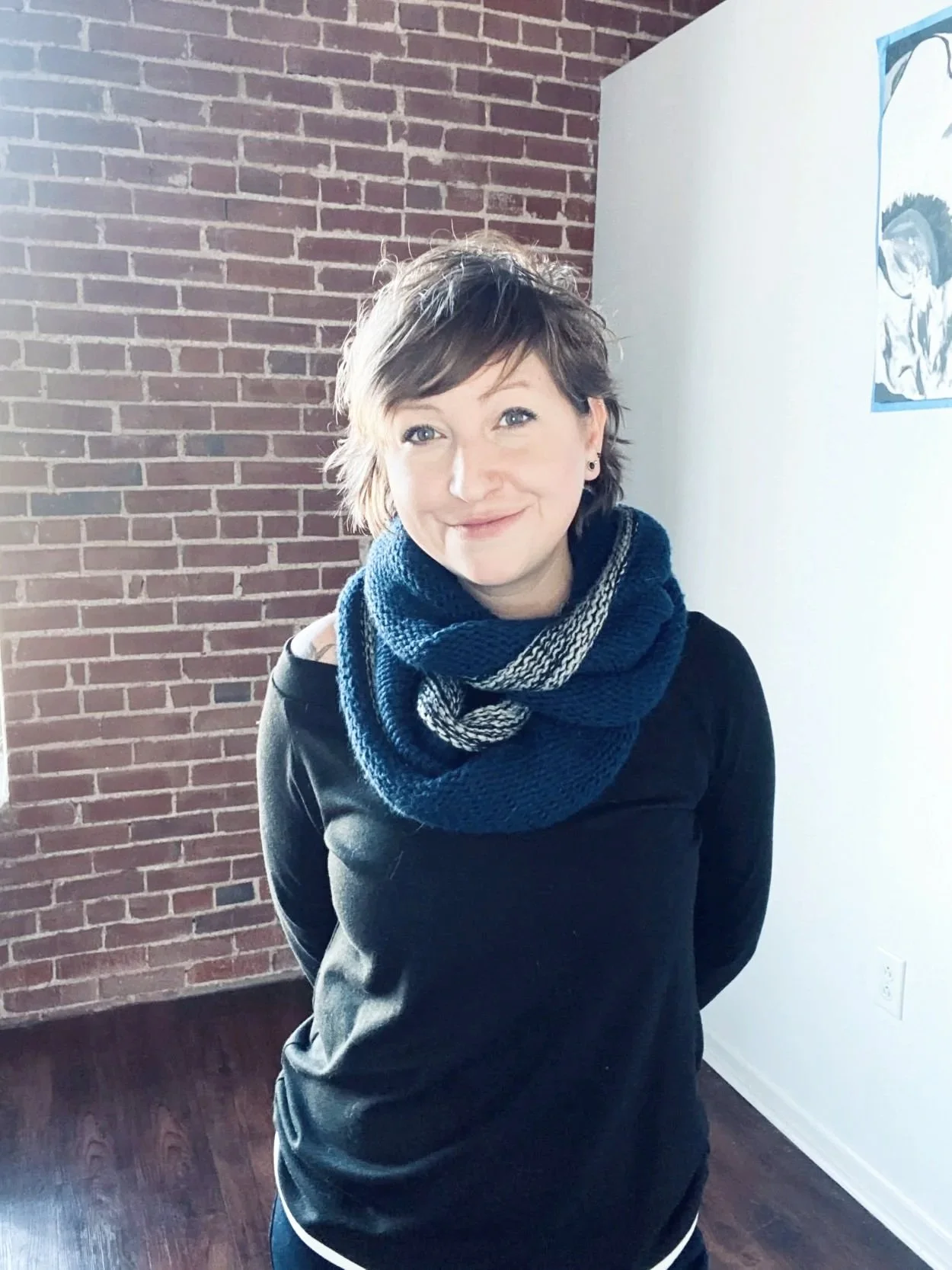 Dr. Jenny stands in front of a brick wall, wearing a chunky scarf, sweater, and smile.