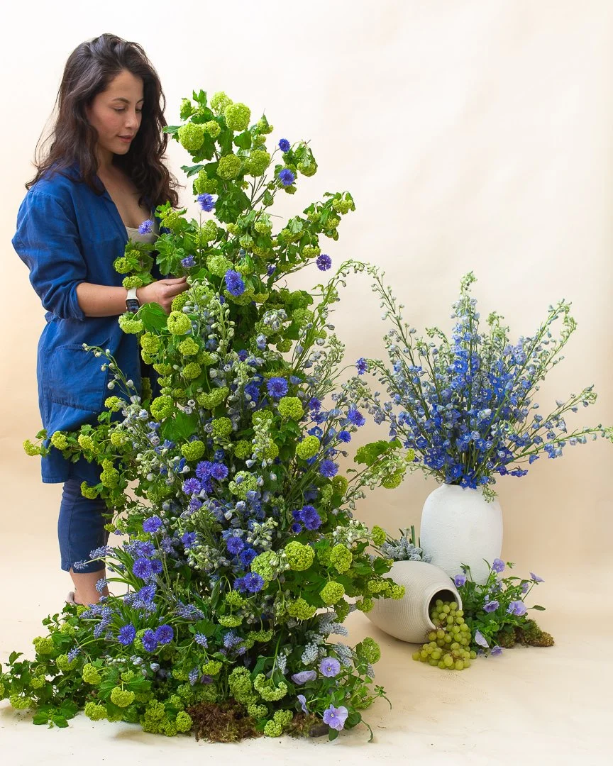 Lucy Blooms designs floral installation in green and blue color palette including seasonal spring flowers, viburnum branches, muscari, pansies, blue delphinium, and blue bachelor buttons