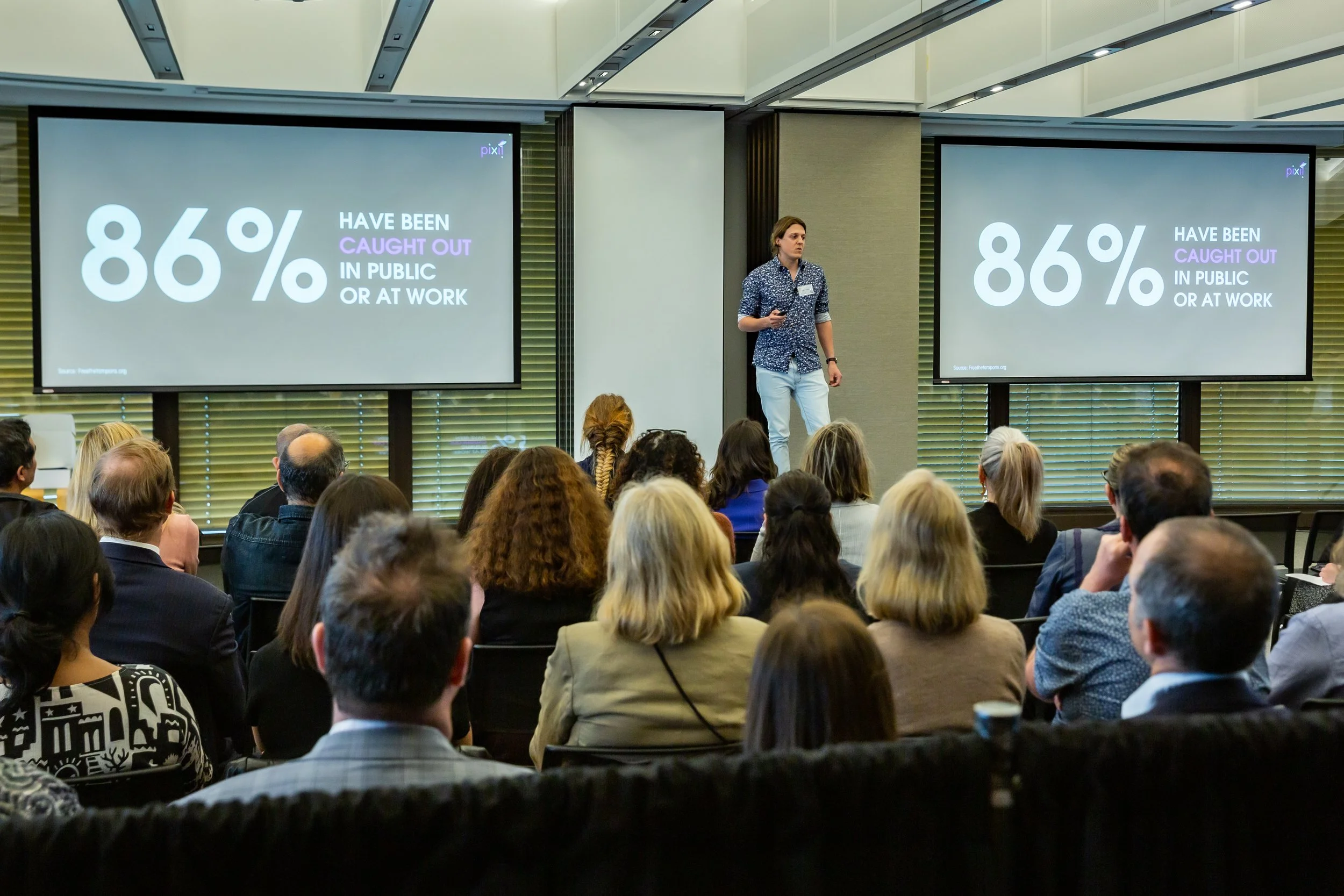 A speaker standing on a stage in front of a seated audience during a presentation, with two large screens displaying the statistic '86% HAVE BEEN CAUGHT OUT IN PUBLIC OR AT WORK' in bold white and purple text on a dark background.
