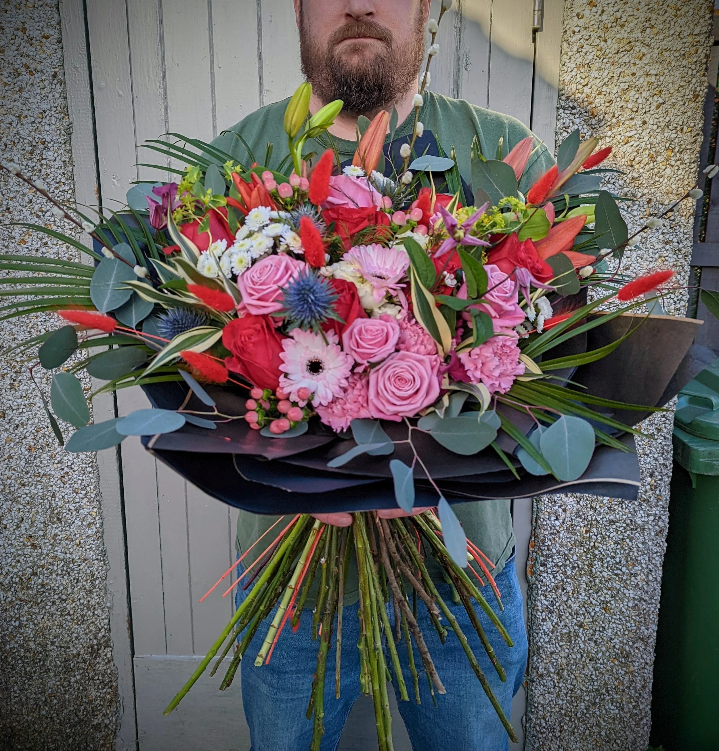 Person holding a large colorful bouquet of pink, red, purple, and blue flowers outdoors.