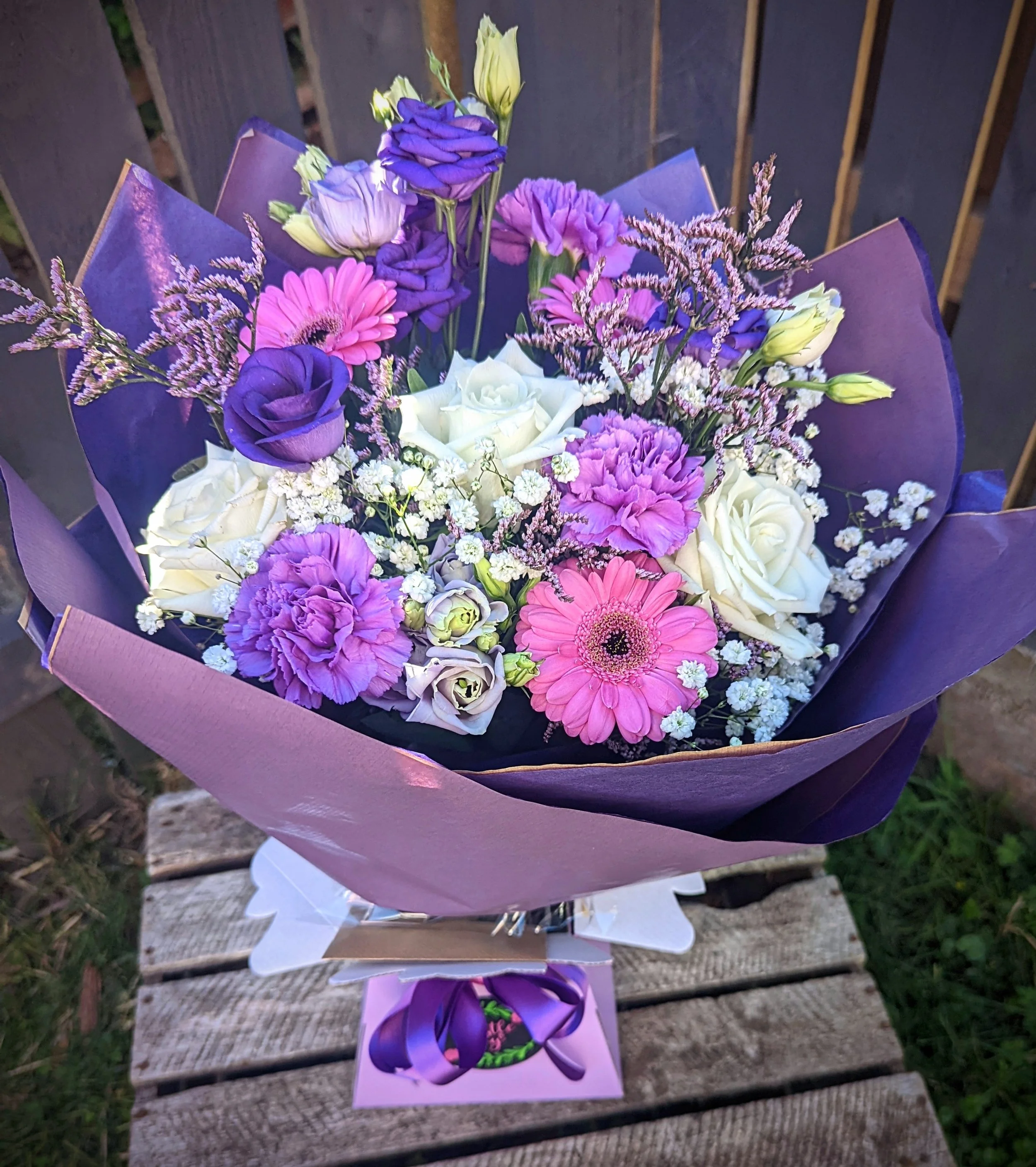 Bouquet of purple, pink, and white flowers wrapped in purple paper and placed on a wooden surface