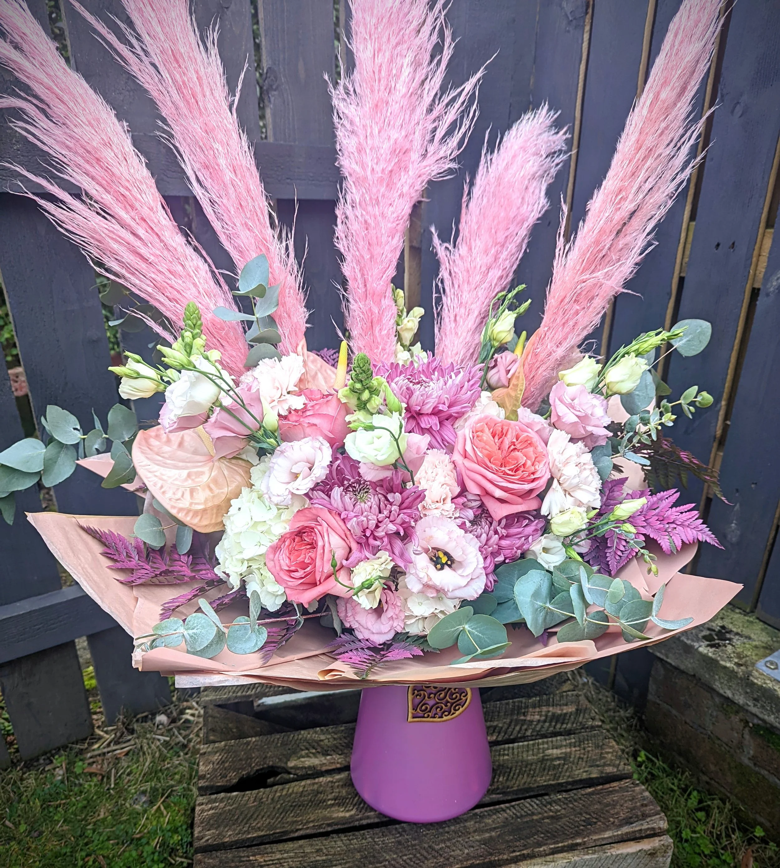 Pink and purple floral arrangement with pampas grass in a purple vase