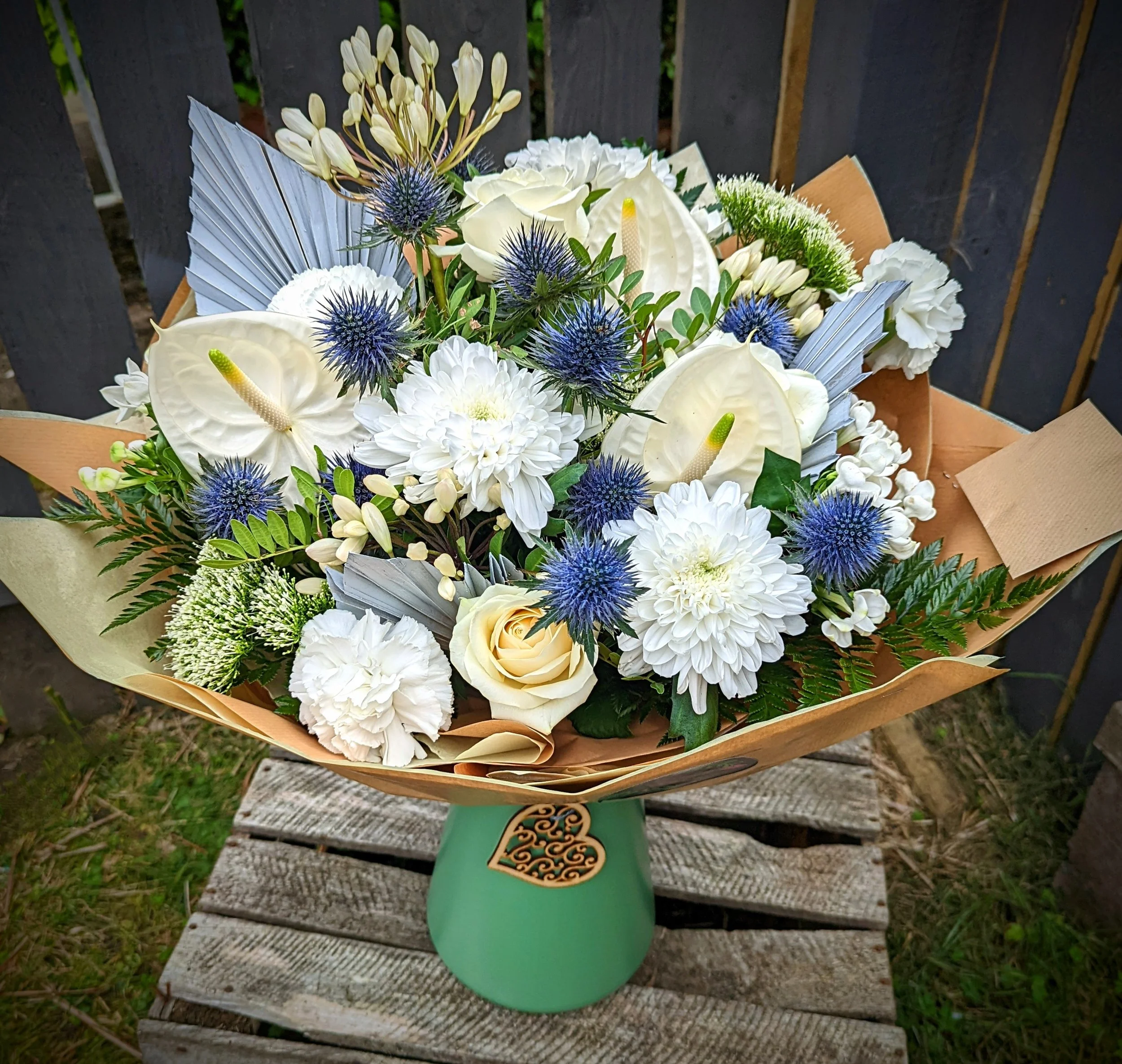 A bouquet of white and cream-colored flowers including roses, dahlias, cremones, and greenery arranged in a green vase.