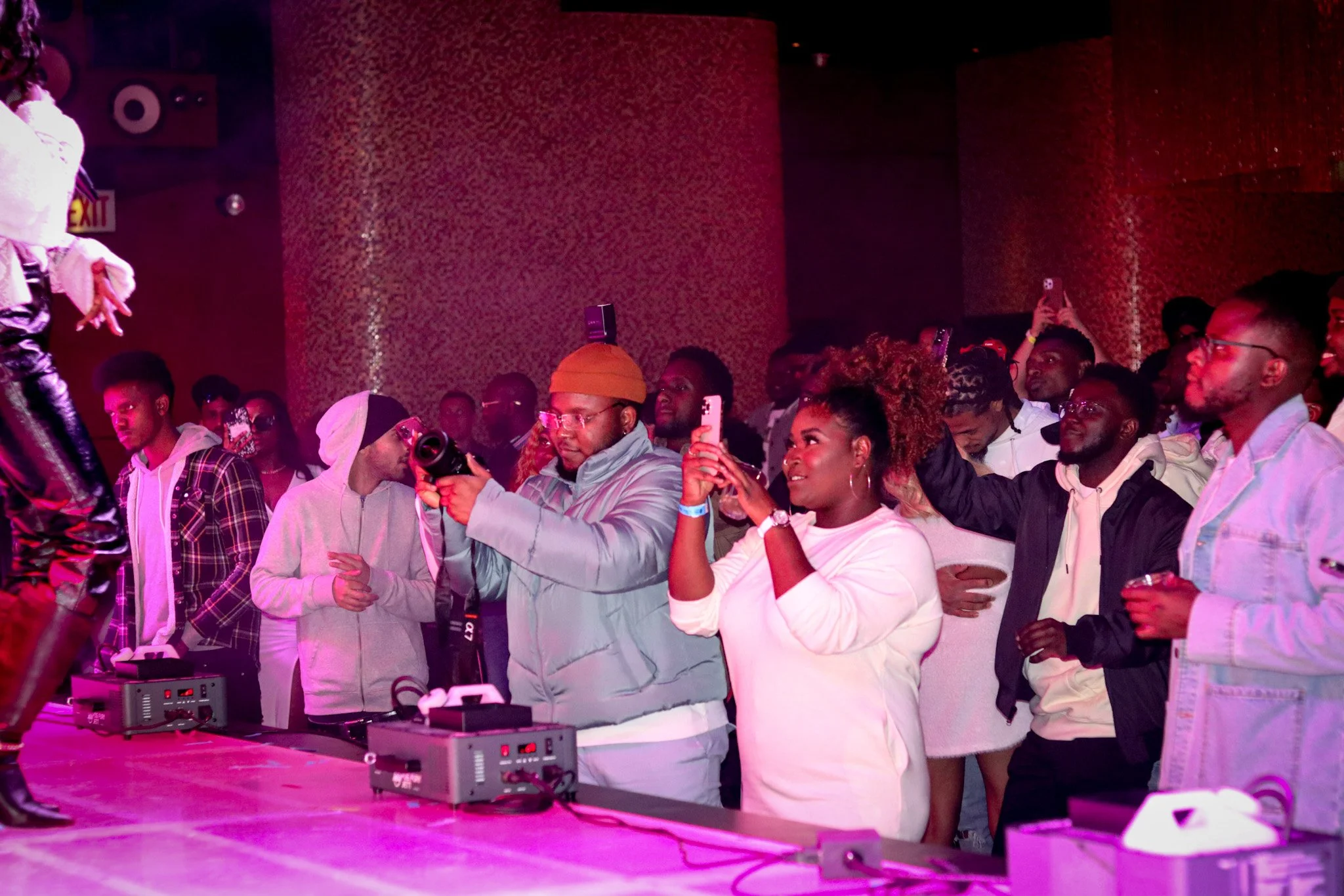 A group of people at a concert or event, with some taking photos or videos and others watching a performer.