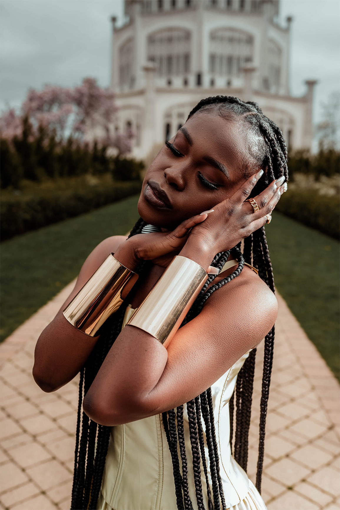 Queen Drie in a royal gown and a gold arm cuff, standing at the Bahai House of Worship in May 2022