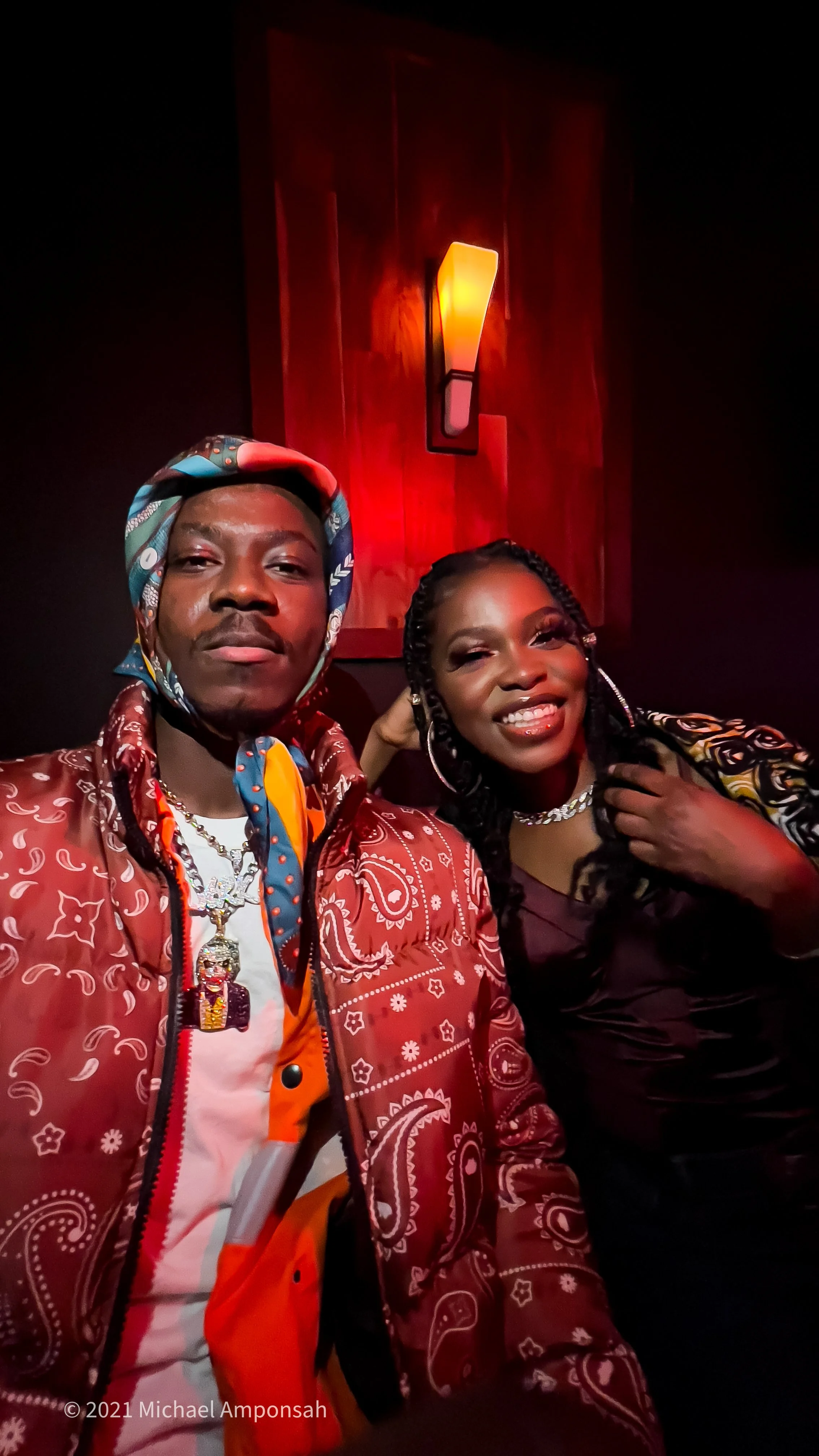 Two people taking a selfie, indoors with a dark background and warm lighting.