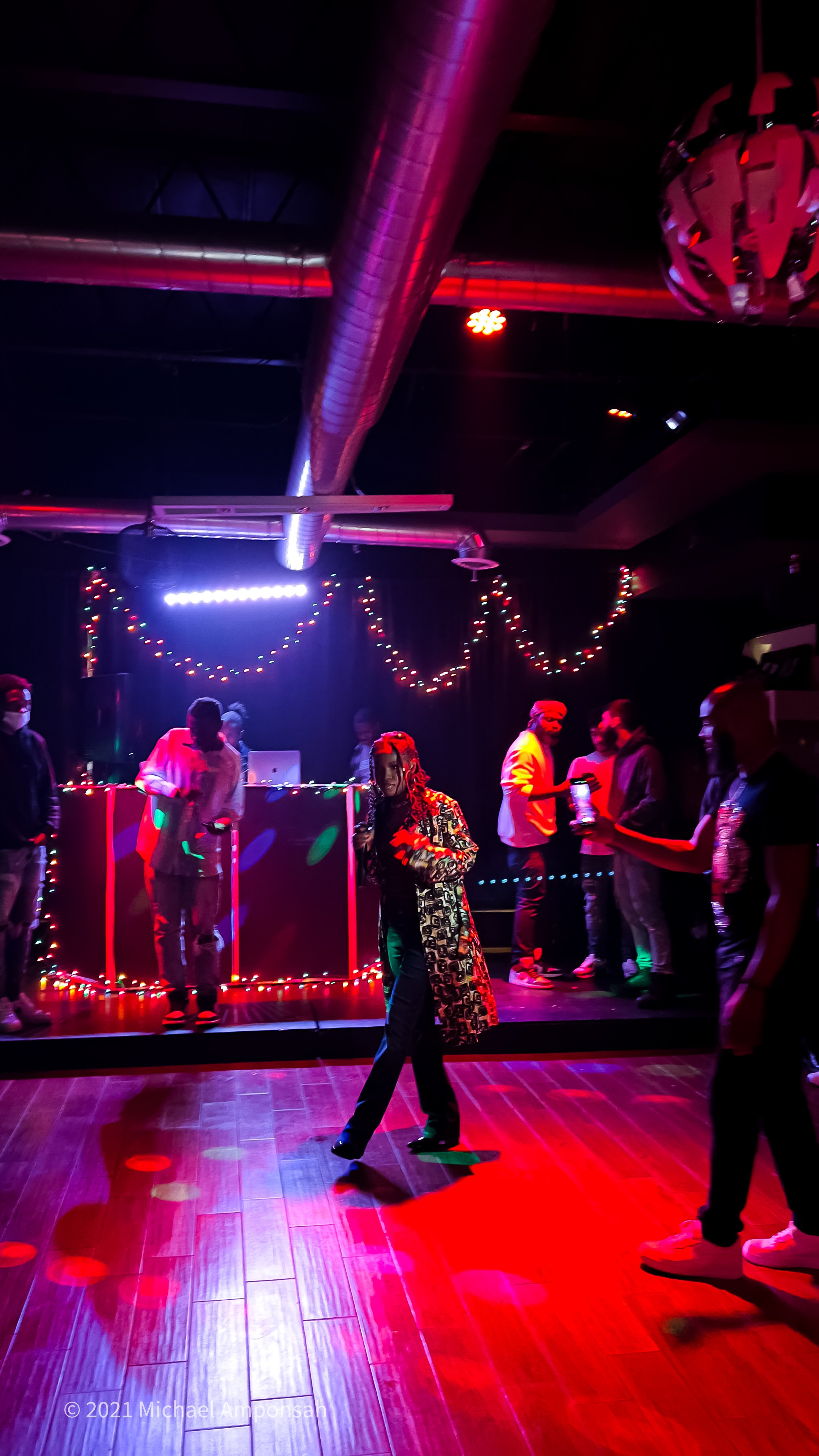 People dancing and socializing at a nightclub with colorful lights, a DJ booth, and Christmas decorations.