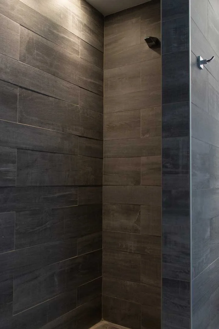 Empty shower with dark gray tiled walls and a wall-mounted showerhead.
