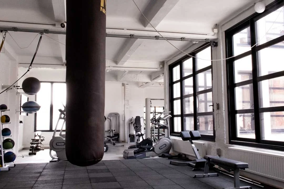 Empty gym with exercise equipment, large windows, and a punching bag.