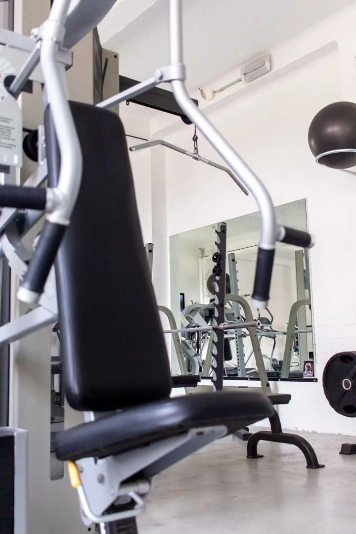 A gym with exercise machines, weightlifting equipment, a mirror, and a black spherical light fixture on the ceiling.
