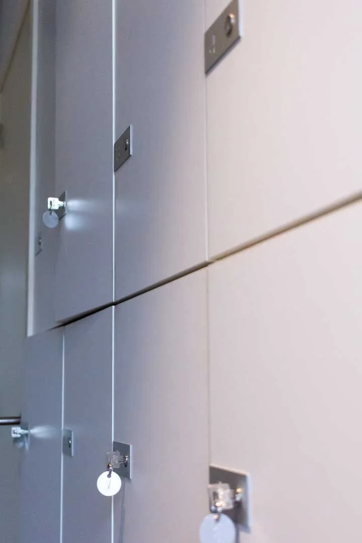 Close-up of a row of grey lockers with small locks, some with key tags, in a public or school setting.