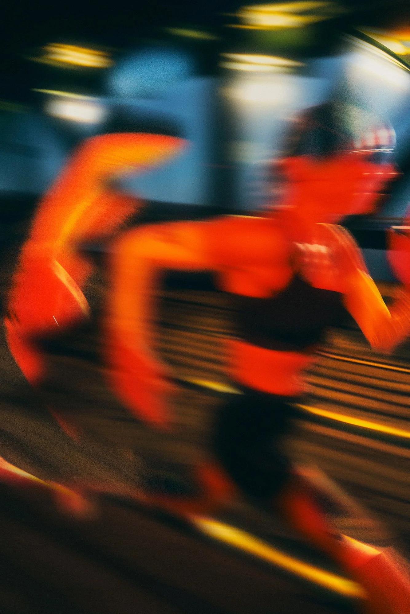 Blurry image of a person riding a roller coaster at night, with orange and red colors on the ride and streaks of light.
