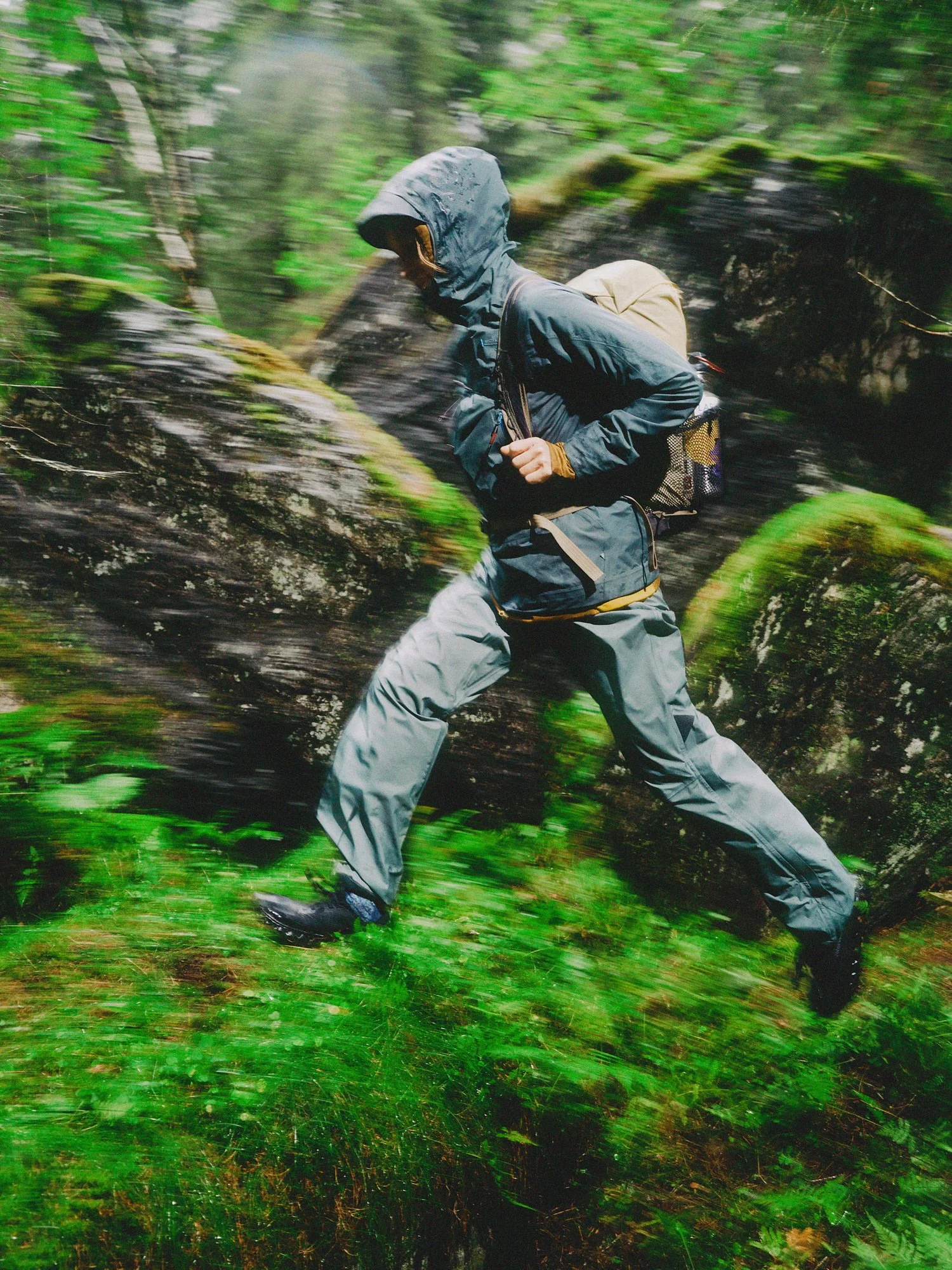 A hiker dressed in gray outdoor gear running through a lush, green forest.