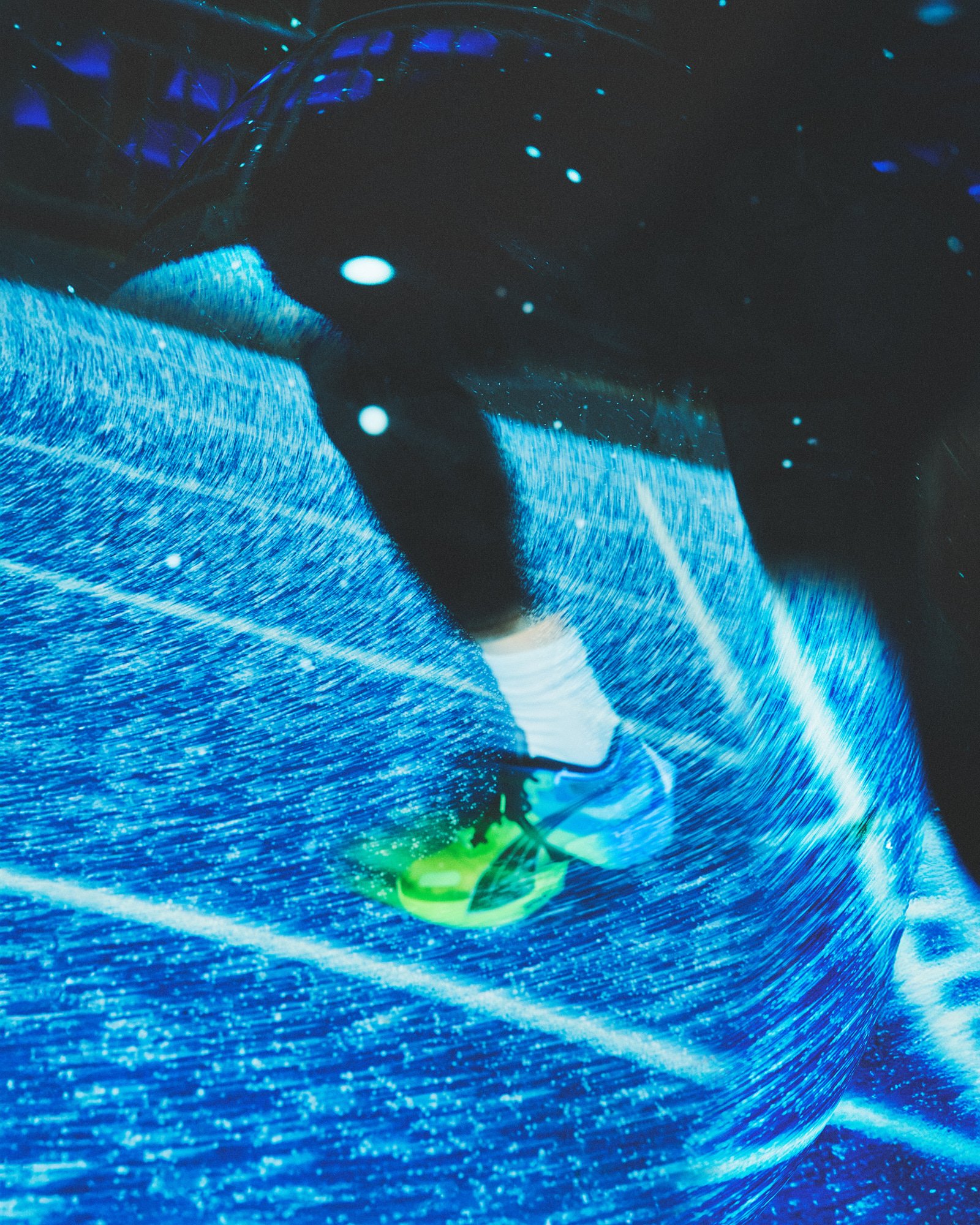 Close-up of a person riding a hoverboard over an LED-illuminated surface, with a neon green shoe visible, in a dark setting with blue light.
