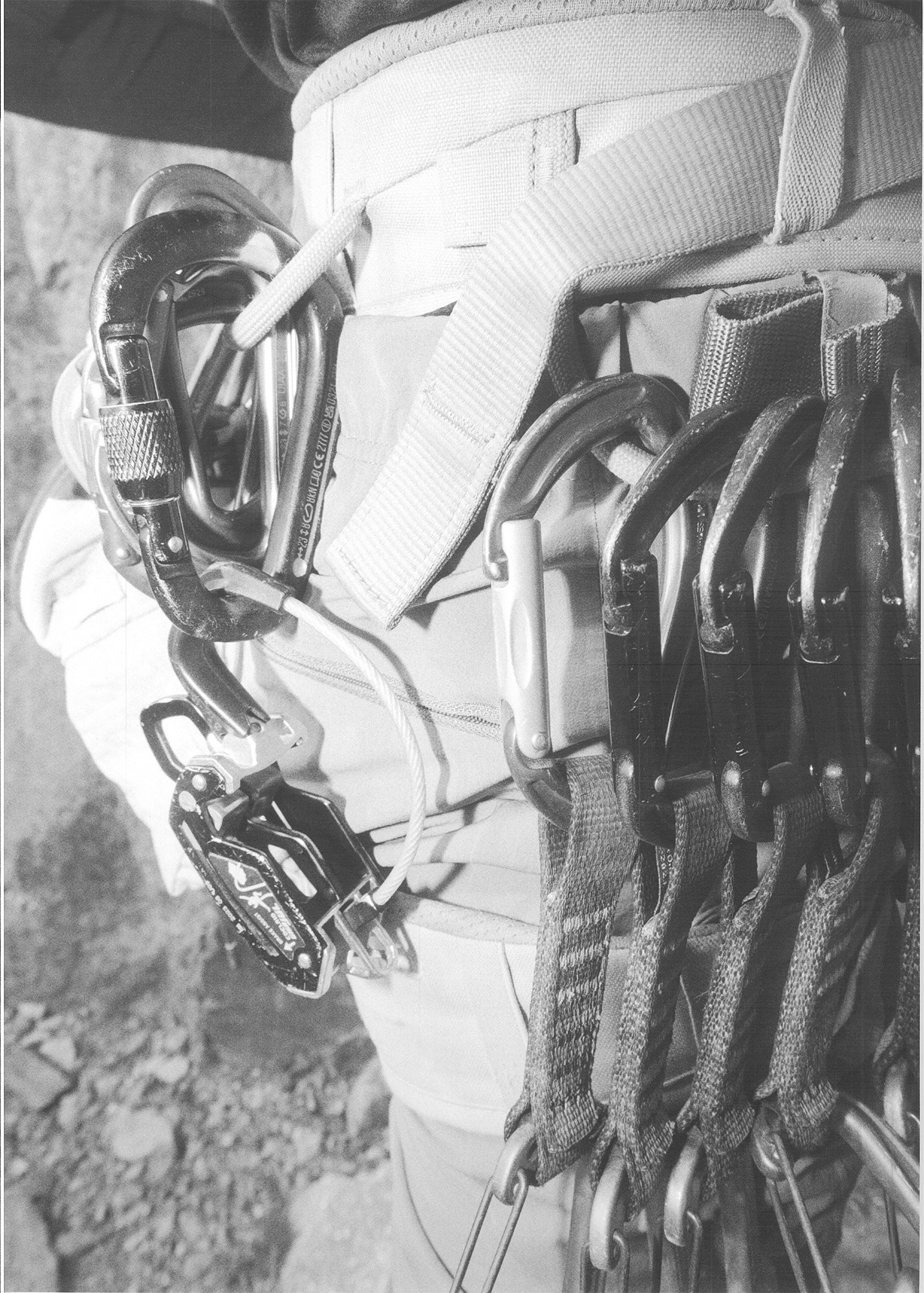 Climber's harness with carabiners, quickdraws, and climbing gear attached, outdoor setting.
