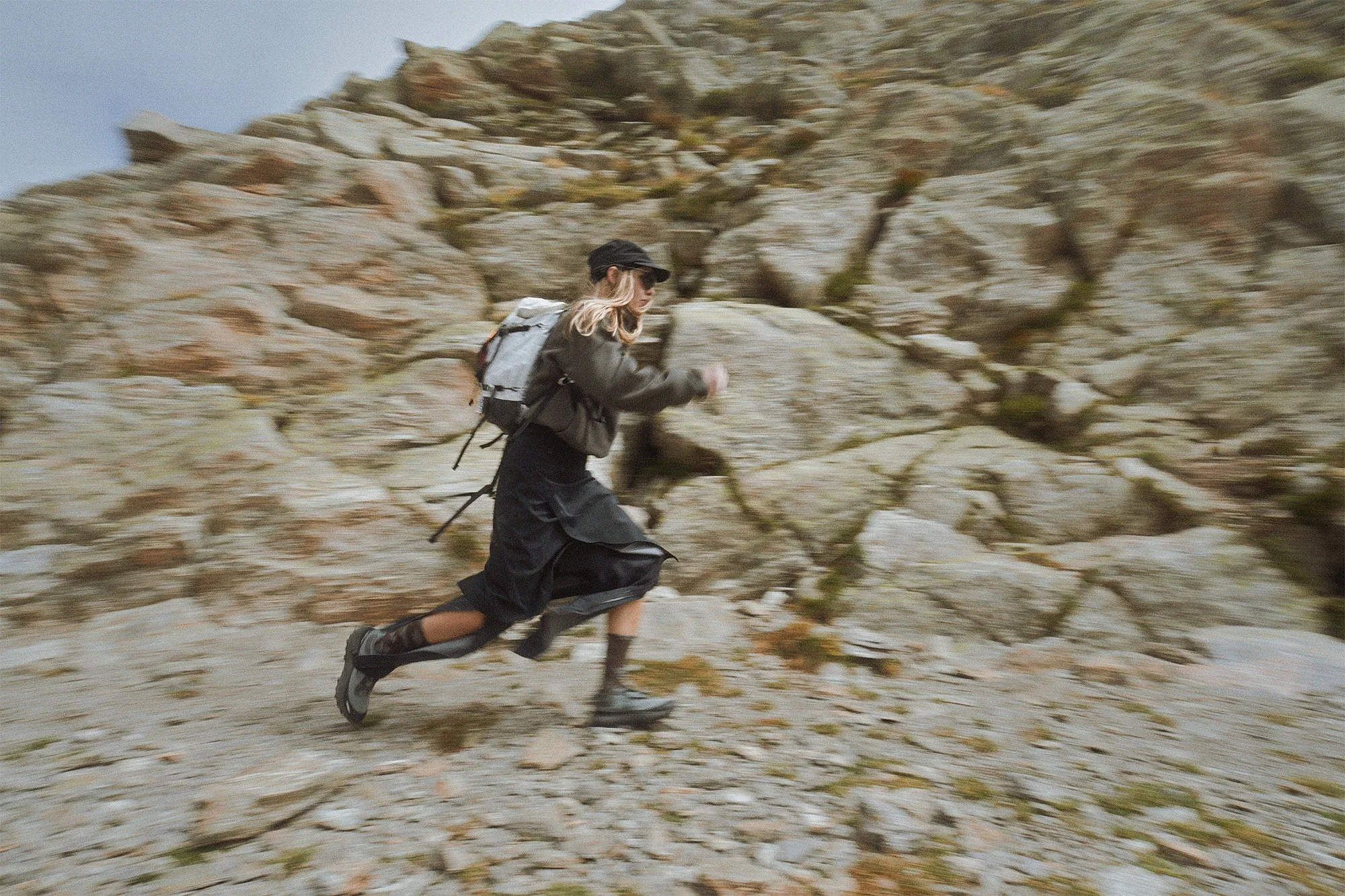 A person hiking up a rocky mountain trail with a backpack and walking sticks.