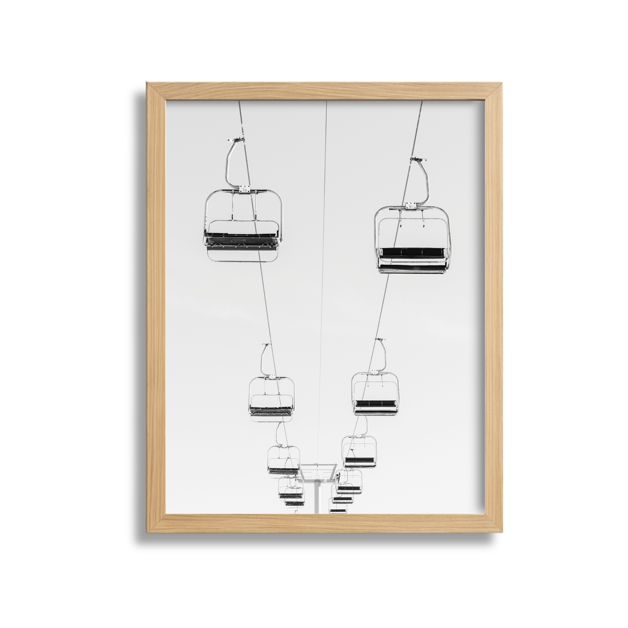Black and white photograph of empty ski lift chairs suspended in the air, viewed from below against a plain sky background.