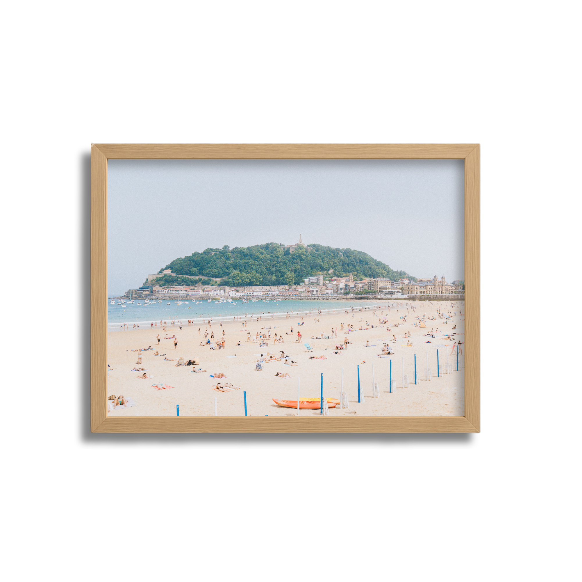 Framed photograph of a beach with people sunbathing and swimming, with a green hilly island and cityscape in the background.