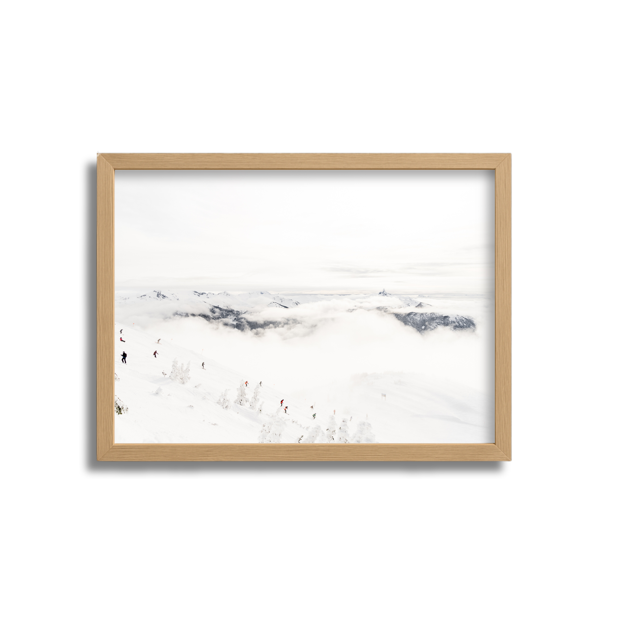 A framed photo of a snowy mountain landscape with skiers descending a slope and clouds covering the valley below.