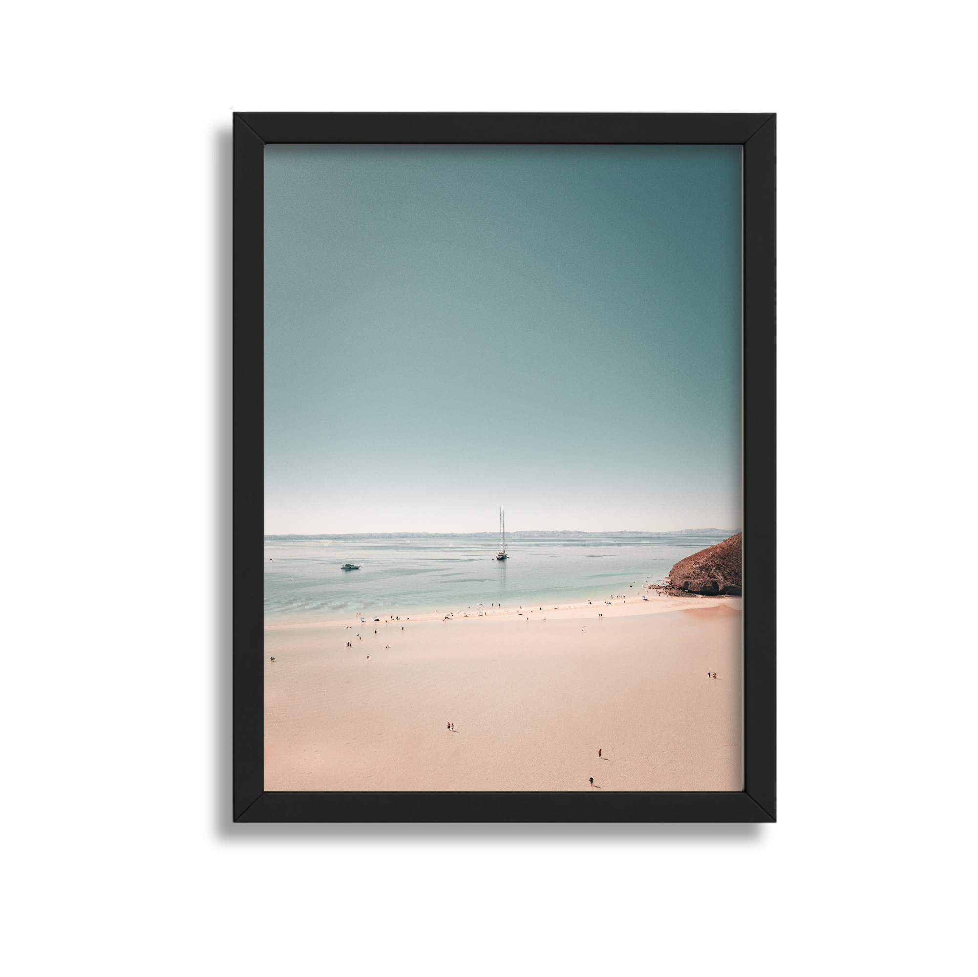Framed photograph of a beach with people, water, and boats under a clear sky.