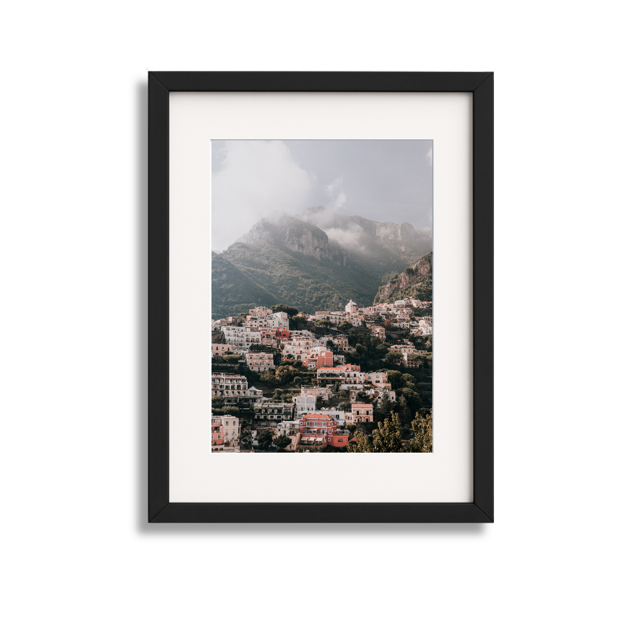 A large framed fine art photography print  scenic view of Positano Italy through a black picture frame, with mountains and cloudy sky in the background with a black frame. 