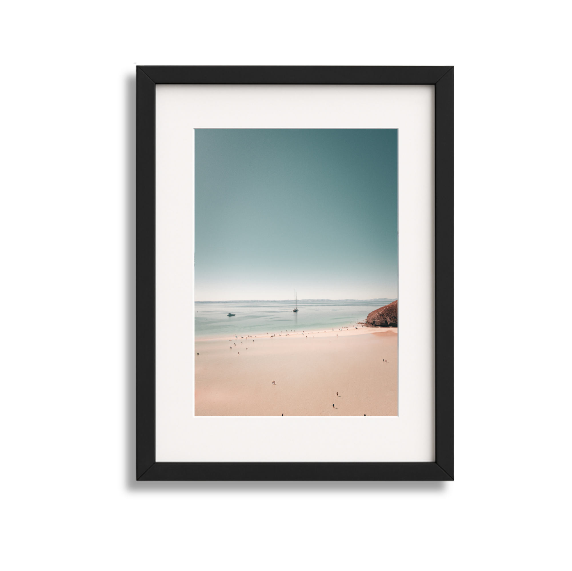 Framed photograph of a beach landscape with gentle waves, boats, and a distant shoreline under a clear sky.